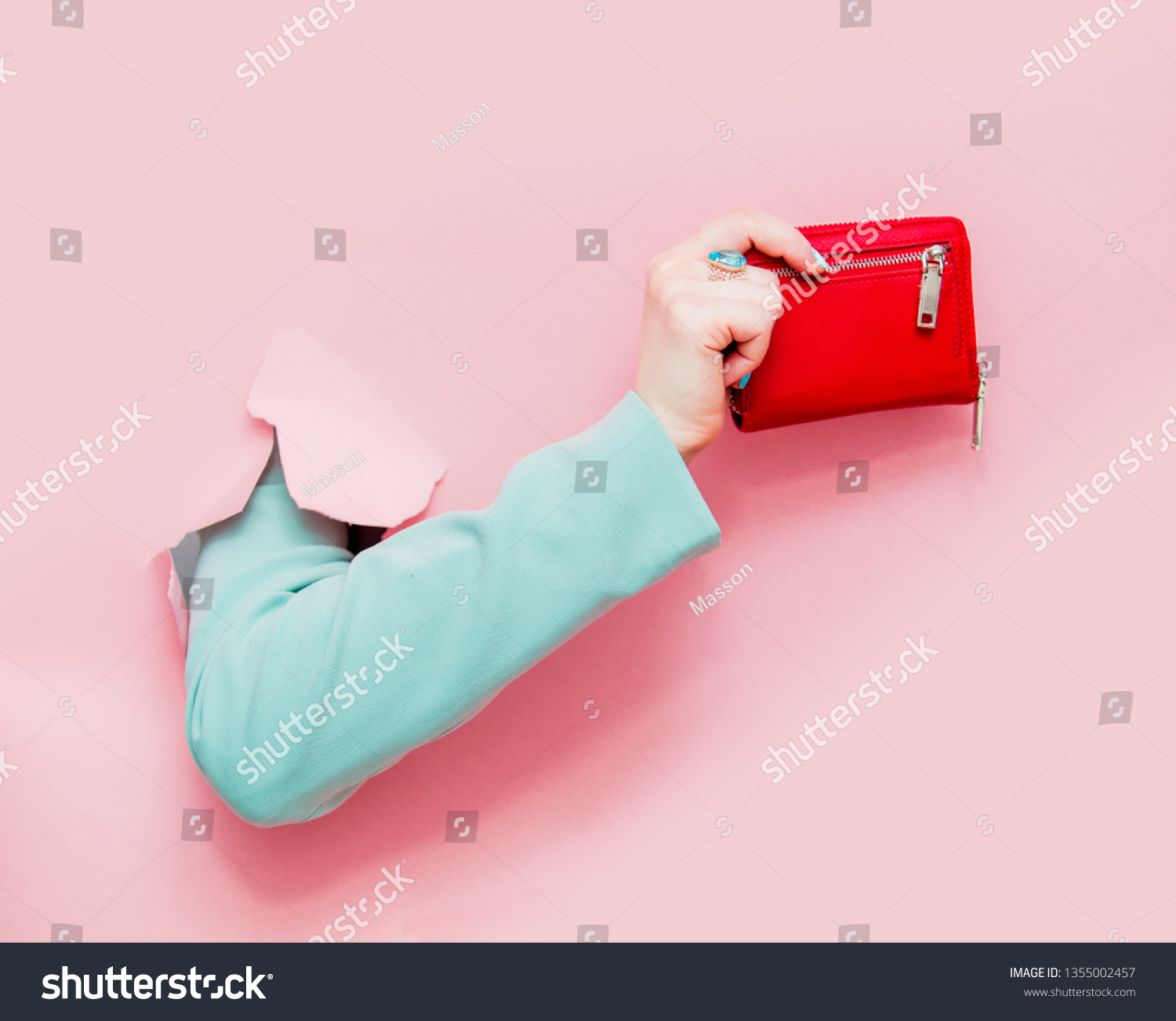 Female hand in classic blue jacket show purse looks out from pink background #1355002457