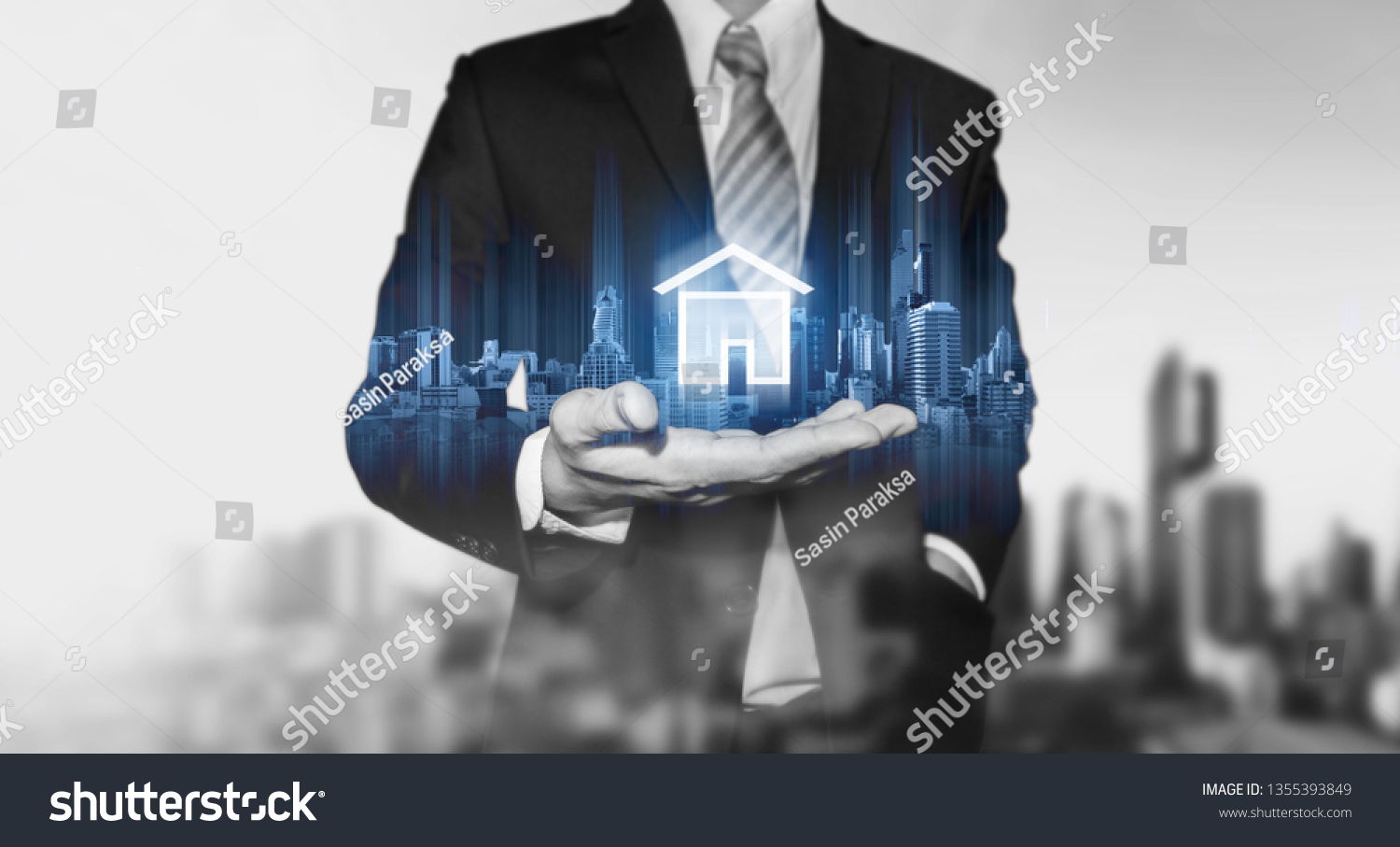 Businessman holding modern buildings hologram, and home icon. Real estate business, building technology and smart home concept #1355393849
