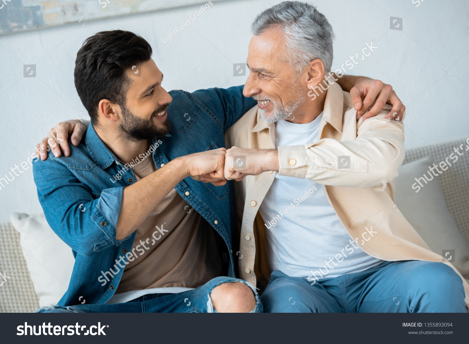 cheerful retired man fist bumping with happy bearded son at home  #1355893094