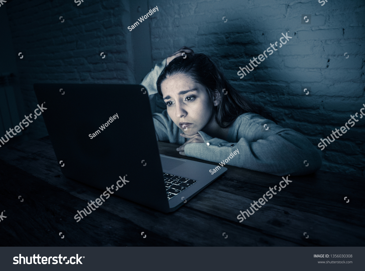 Dramatic portrait of sad scared young woman stressed and worried staring at laptop suffering cyber bullying and harassment. Victim of online abuse and intimidation by stalker. In dangers of internet. #1356030308