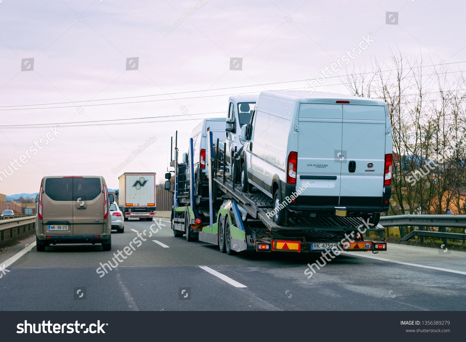 Ljubljana, Slovenia - January 16, 2019: Minivan carrier transporter truck in road. Auto vehicles hauler on driveway. European van transport logistics at haulage work transportation. Haul car trailer #1356389279