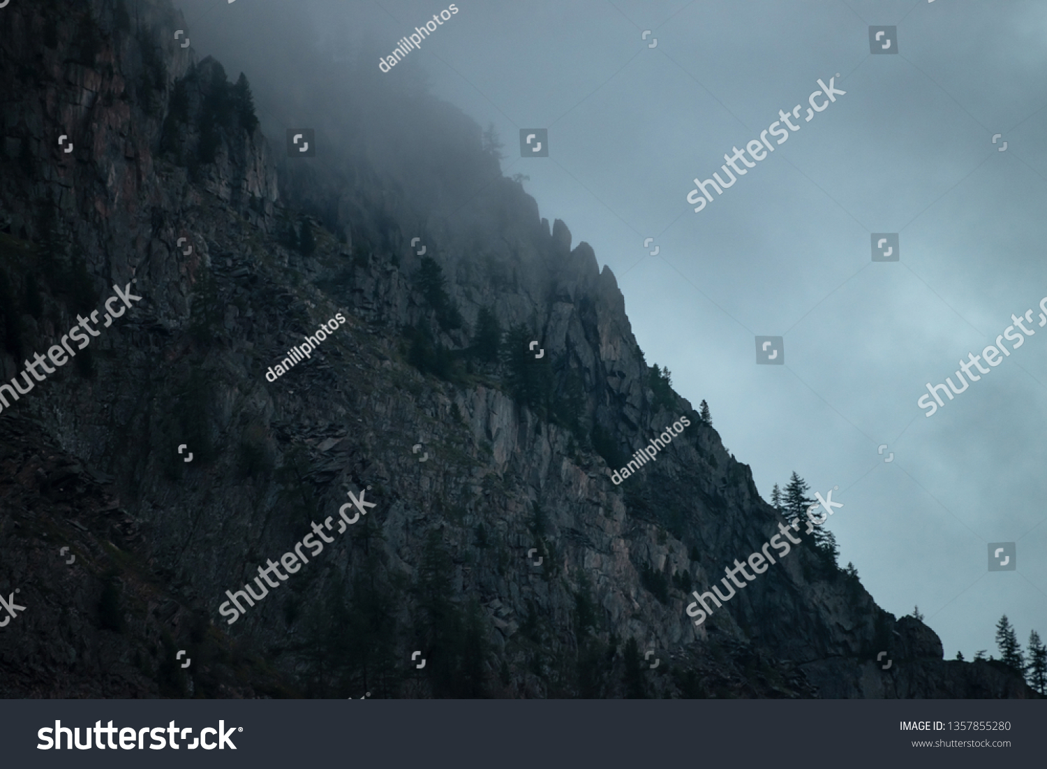 Ghostly giant rocks with trees in thick fog. Mysterious huge mountain in mist. Early morning in mountains. Impenetrable fog. Dark atmospheric eerie landscape. Tranquil mystic atmosphere of wilderness. #1357855280