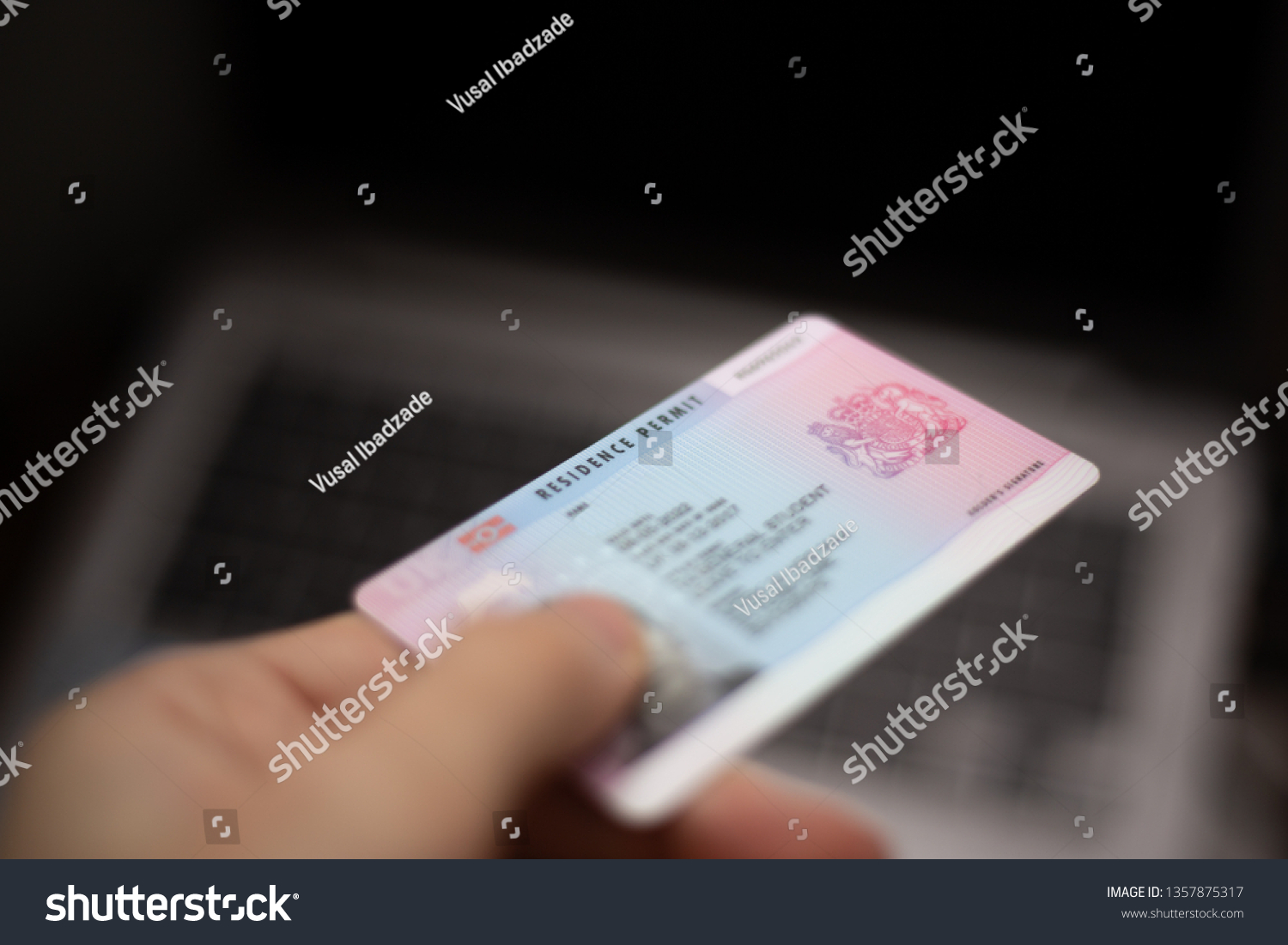Person holds UK Residence Permit - BRP card in hand and computer in the background. Immigration concept image.  #1357875317