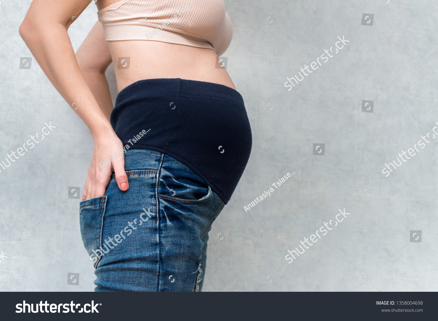 Pregnant woman in maternity pants. Pants with a rubber band on the abdomen. Belly closeup. Gray background. Free space #1358004698