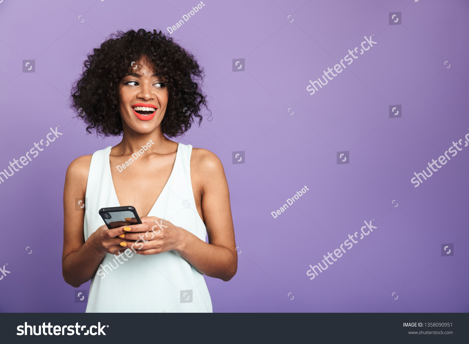 Happy pretty african woman holding smartphone and looking away over violet background #1358090951