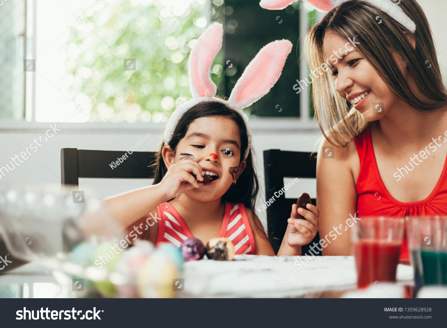 Happy easter! A mother and her daughter painting Easter eggs. Happy family preparing for Easter. Cute little child girl wearing bunny ears on Easter day #1359628928