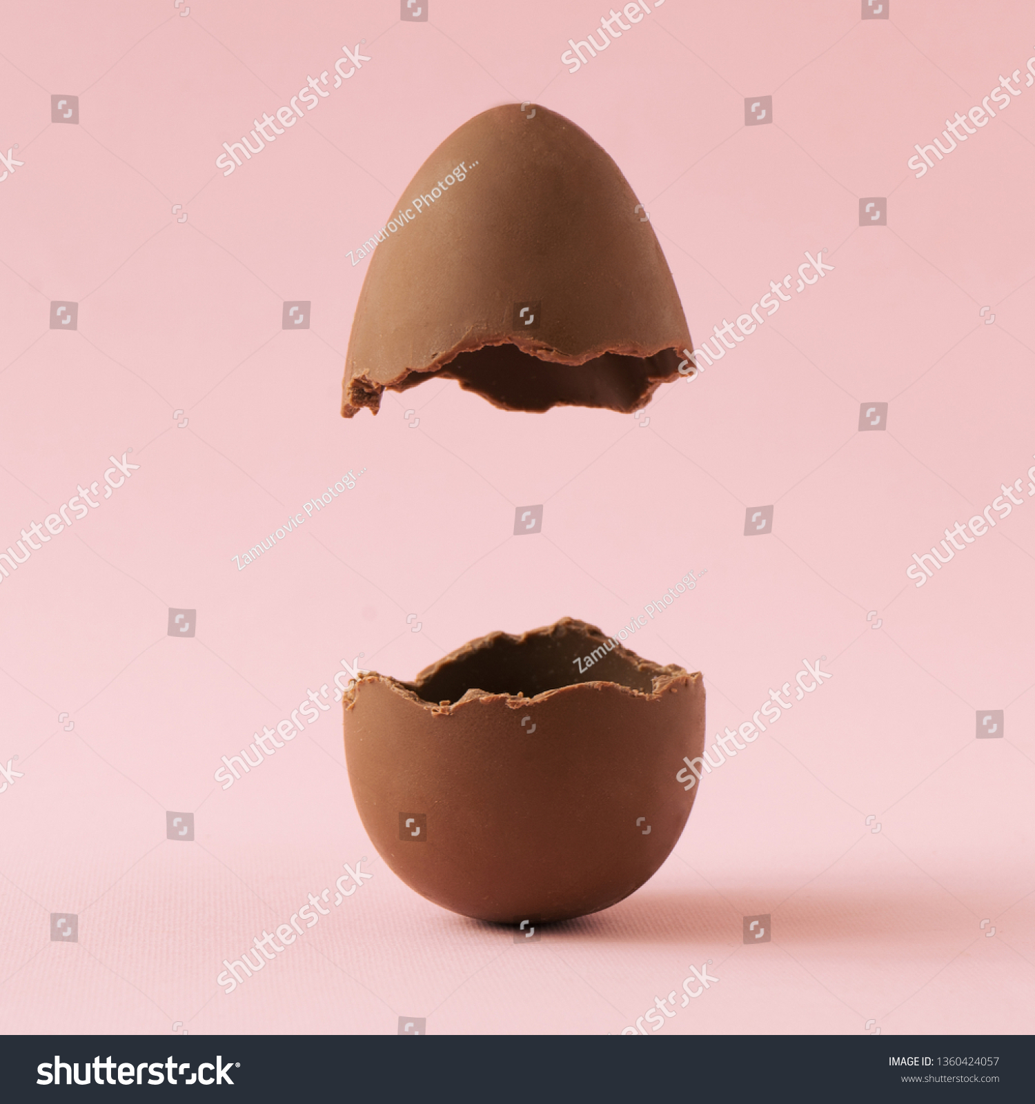 Chocolate Easter egg broken in half on pastel pink background with creative copy space. Minimal Easter holiday concept. #1360424057