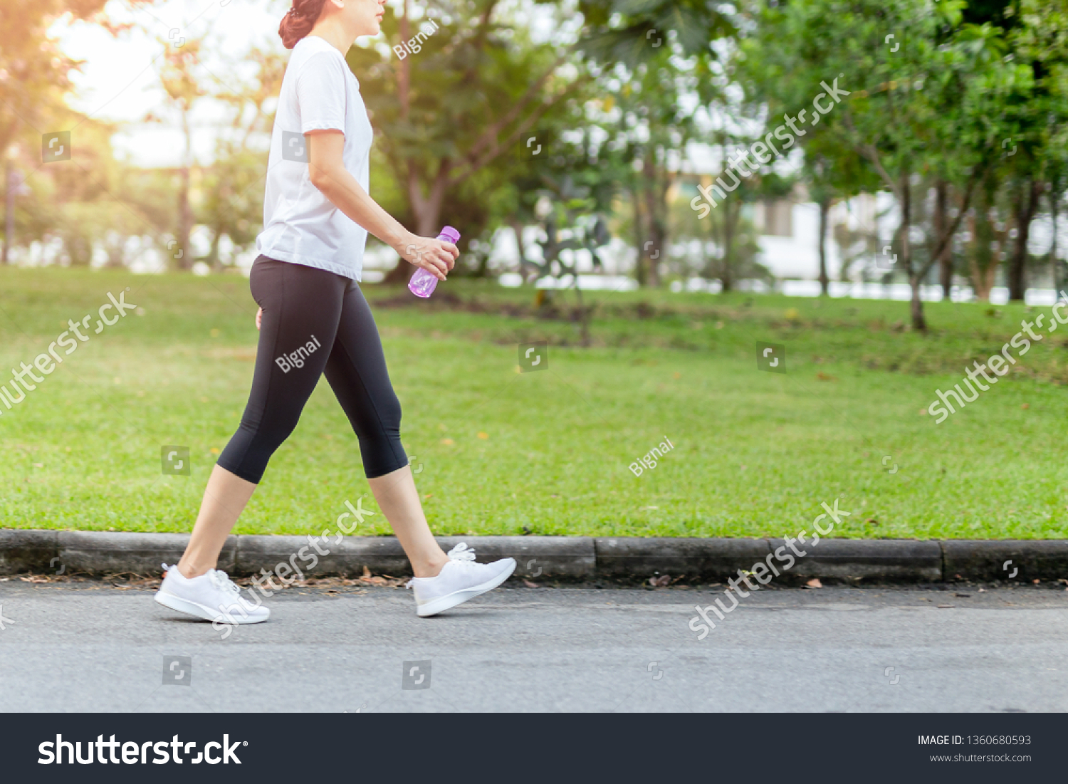 Woman walking in the park with bottle water in summer health care concept. #1360680593