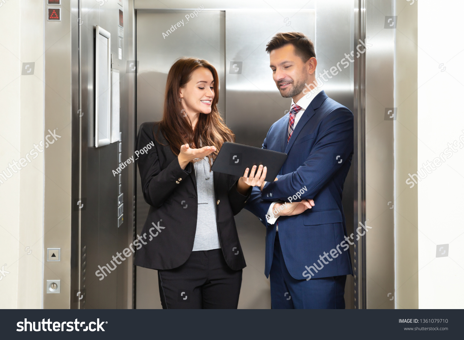 Smiling Young Businesswoman And Businessman Discussing While Using Digital Tablet Standing Near Elevator #1361079710