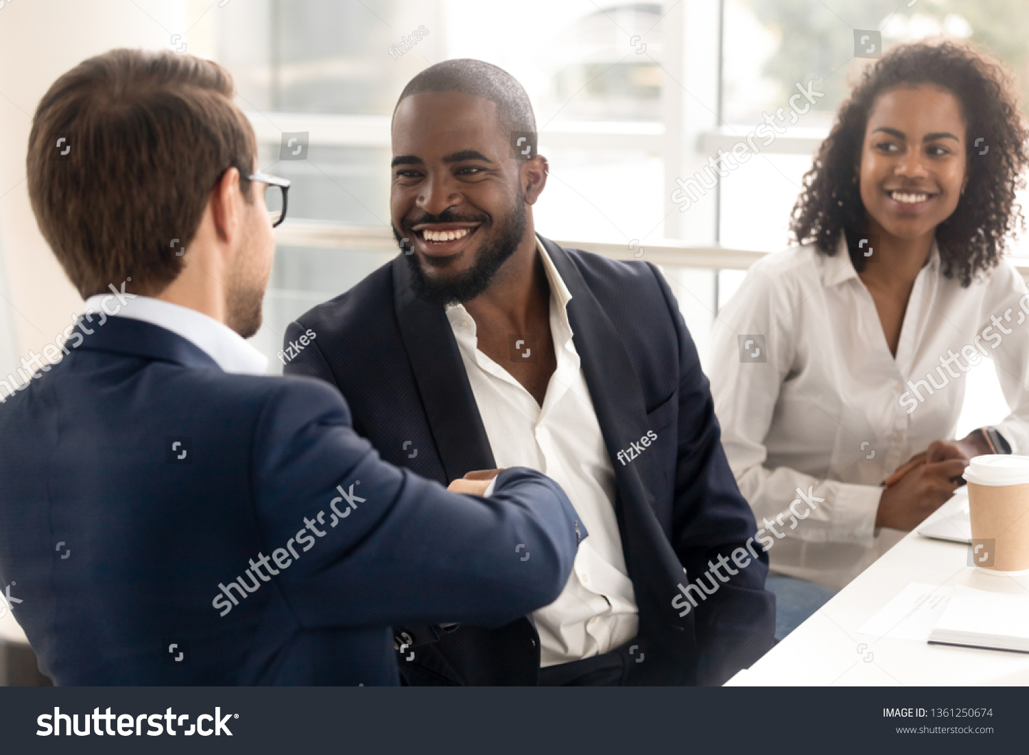 Happy african businessman handshake reliable male partner at team meeting, smiling diverse workers shake hand as respect trust concept, making deal business agreement with client at group negotiation #1361250674