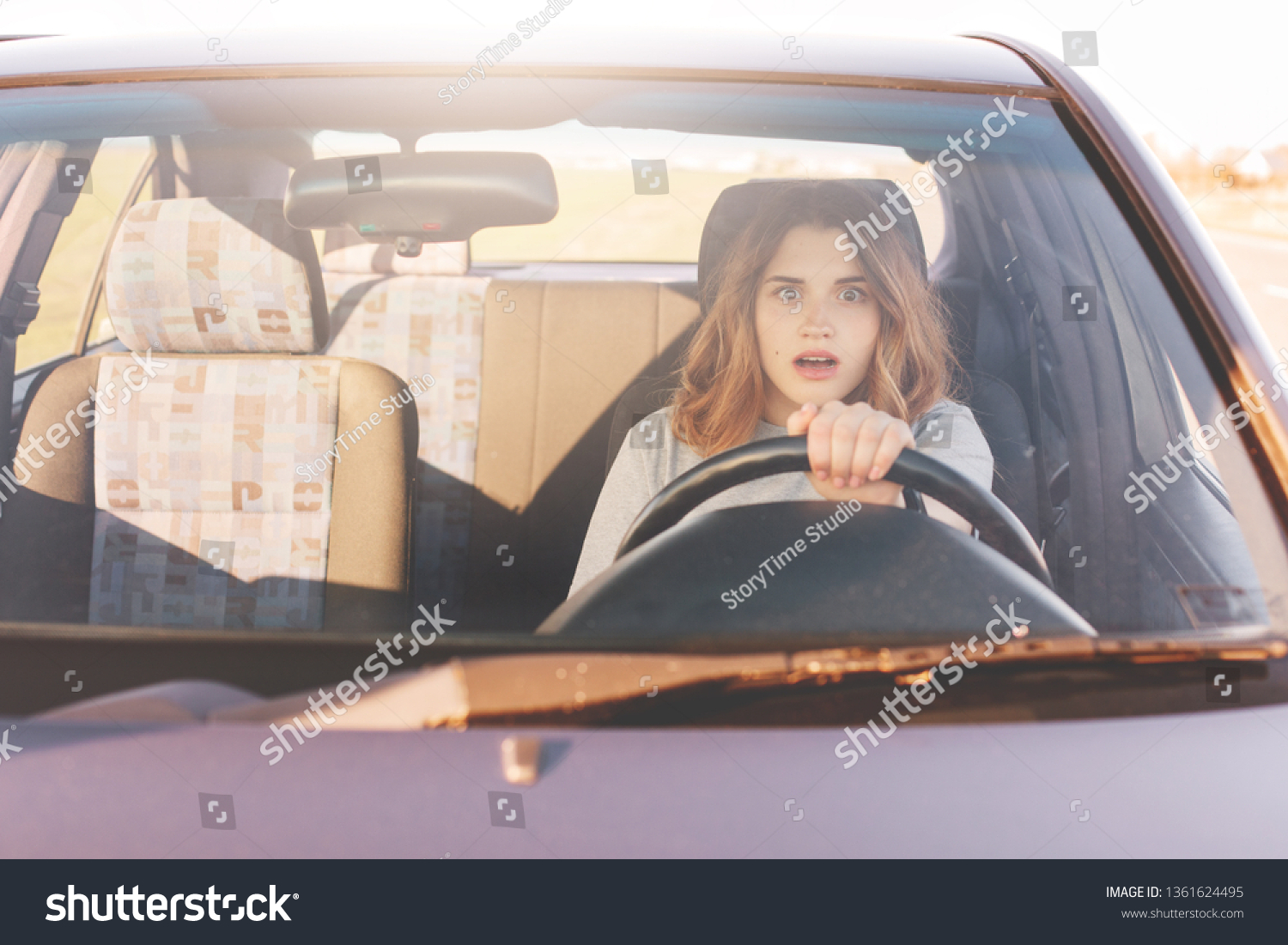 Fearful driving woman, learns to drive automobile, attractive female sits at wheel alone for first time, tries to avoid car accident, has frightened facial experessions, wants to stop vehicle. #1361624495