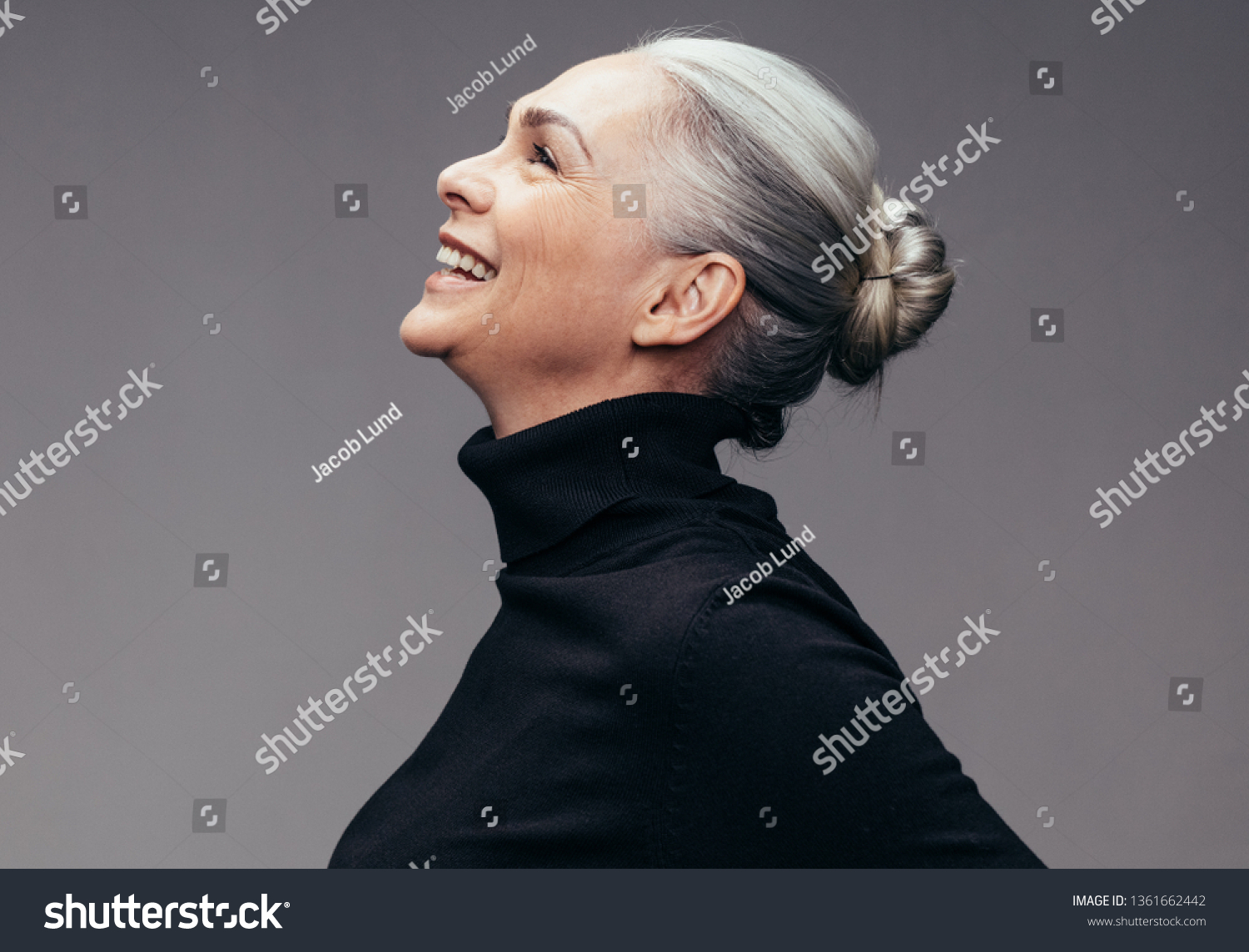 Side view of senior woman laughing on gray background. Profile view of mature woman in black casuals looking happy #1361662442