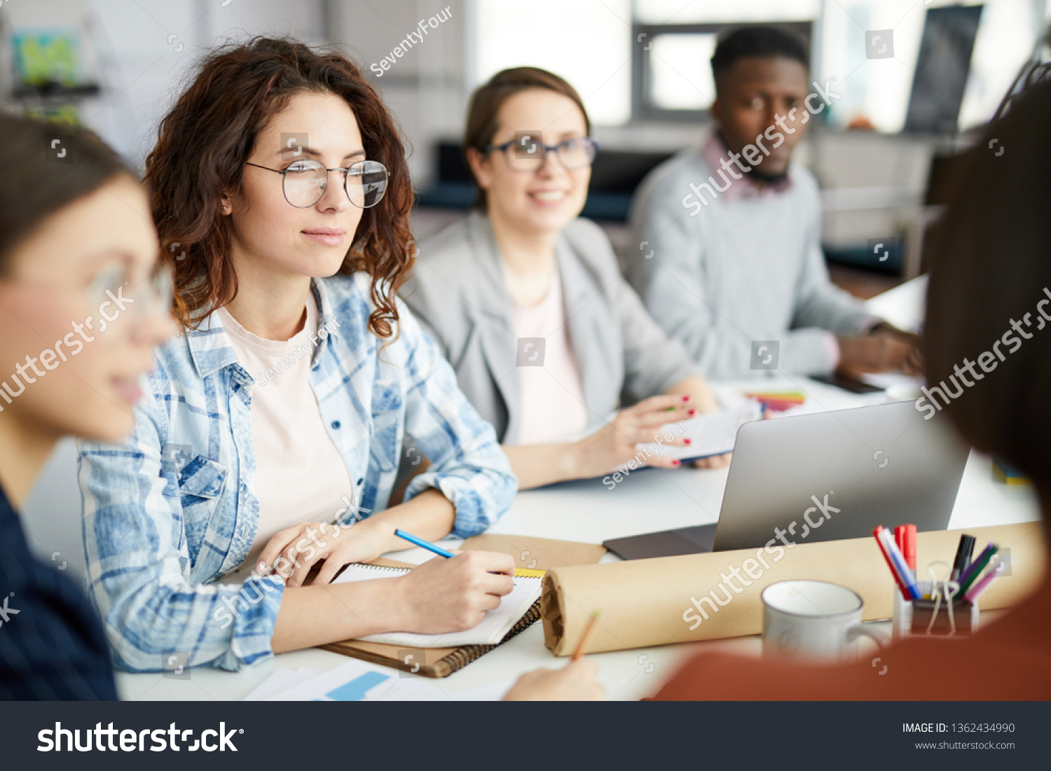Group of contemporary people working in meeting focus on curly haired young woman in foreground, copy space #1362434990