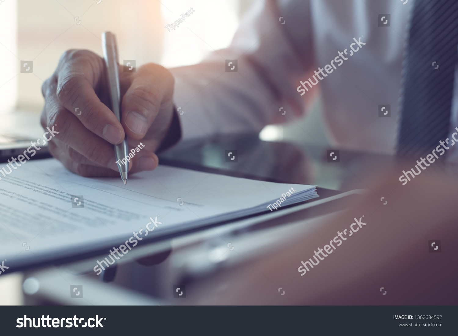 Signing contract, business agreement, deal concept. Business man signing official contract, formal document with a pen and digital tablet computer on desk in office with morning sunlight, close up #1362634592