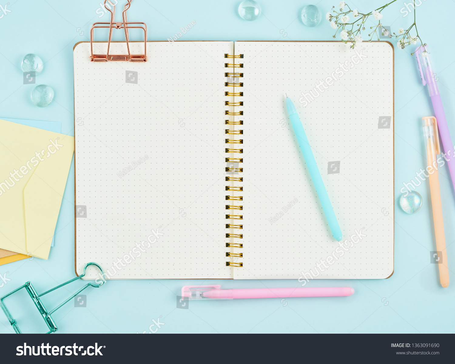 Blank notepad page in bullet journal on blue office desktop. Top view of modern bright table with notebook and flower. Mock up, copy space. #1363091690