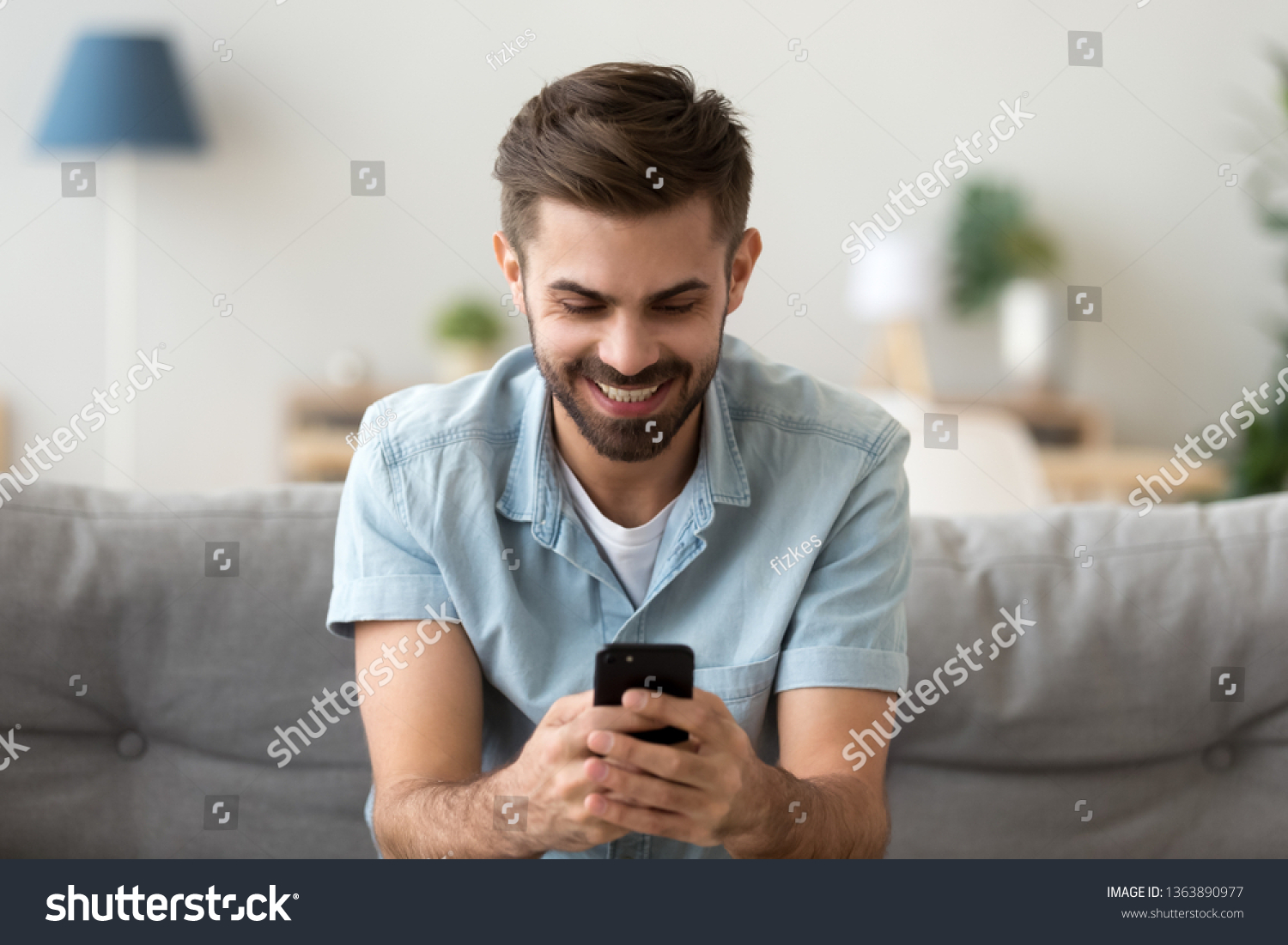 Excited smiling man looking at phone screen, using mobile app, typing message in social network, reading news, email, male student chatting with friends, playing game, watching funny video #1363890977