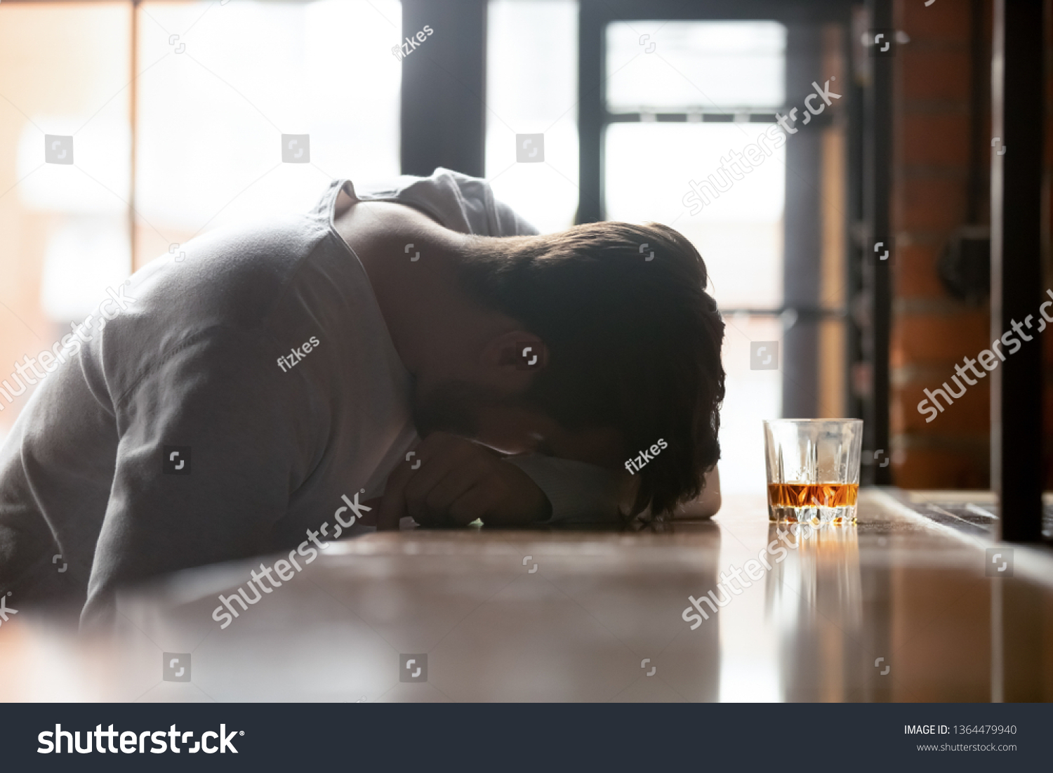 Drunk boozy man sleeping lying on bar counter after drinking large amount of alcoholic beverage glass of whiskey strong booze near him, concept of alcohol use disorder (AUD) alcoholism health problems #1364479940