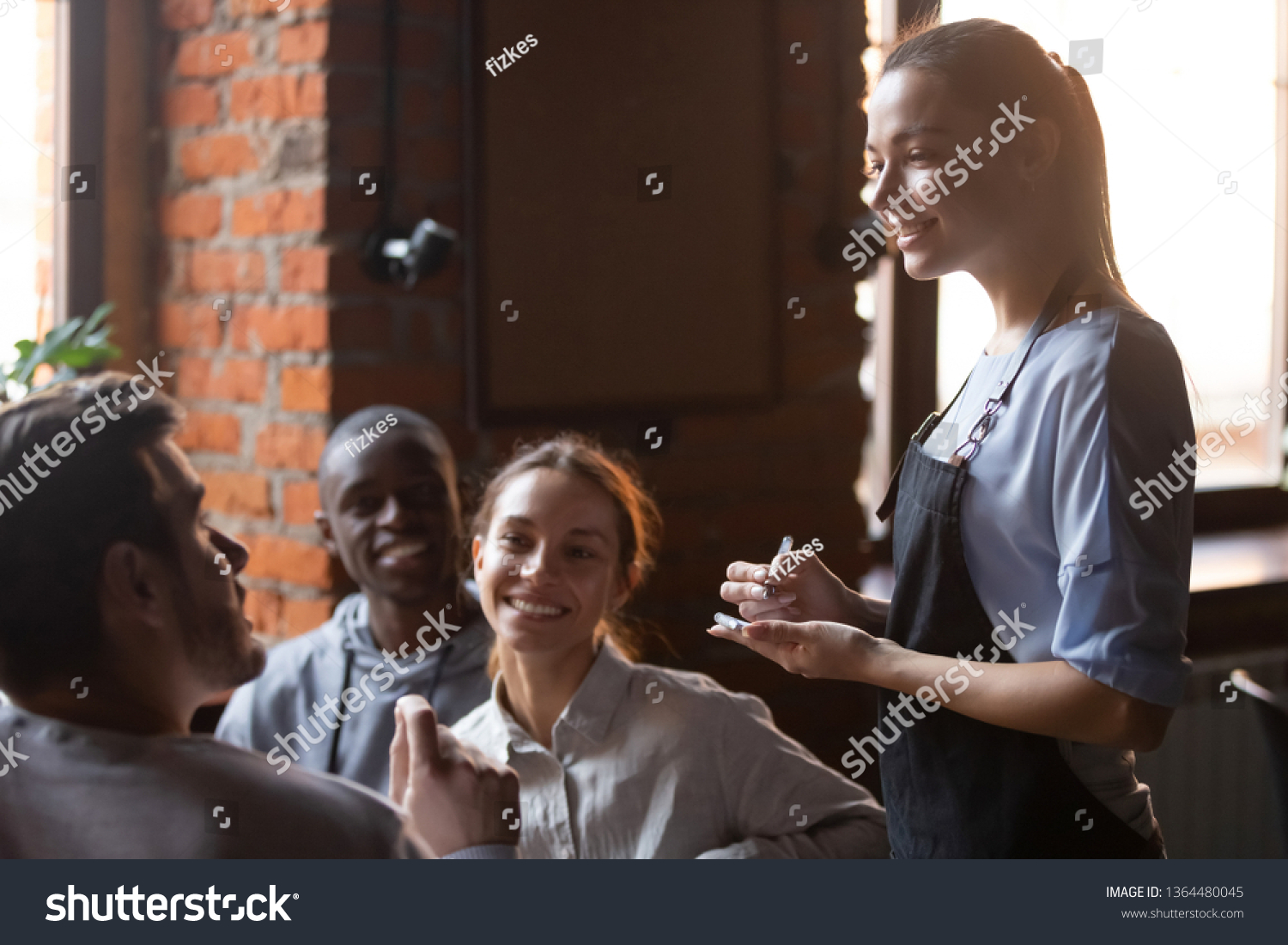Diverse friends gathered together sitting in cafe talking with worker service waiting staff place make order food drink, young waitress business owner listening client wishes writing list in notepad #1364480045