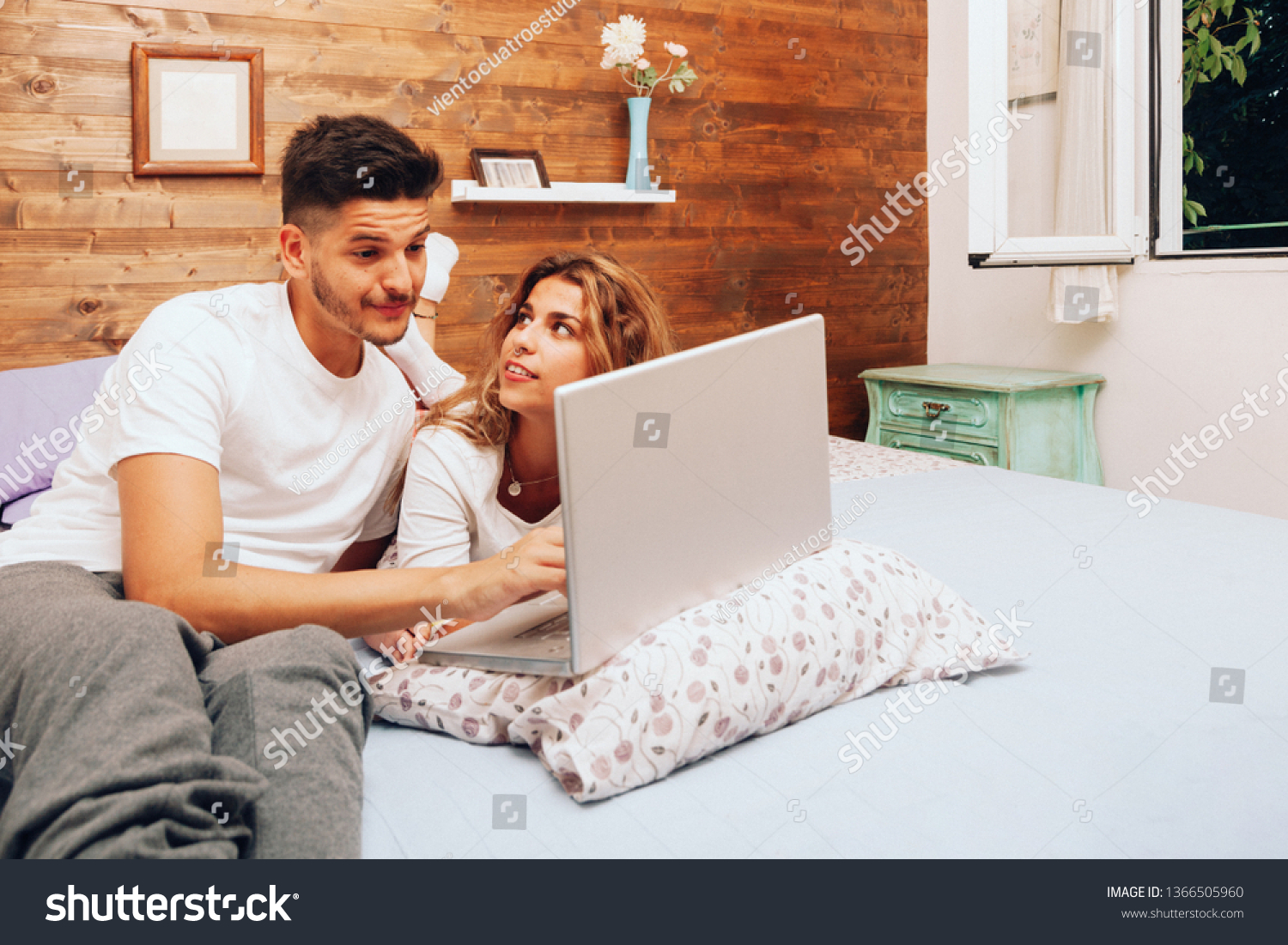 Young smiling heterosexual couple lying down together on the bed using a laptop #1366505960