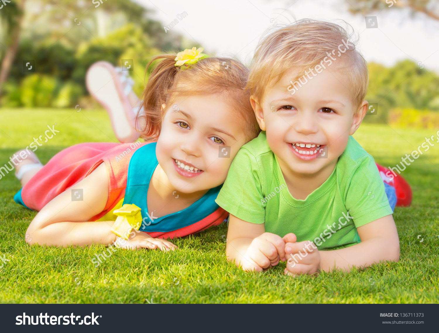 Picture of brother and sister having fun in the park, two cheerful children laying down on green grass, little girl and boy playing outdoors, best friends, happy family, love and happiness concept #136711373