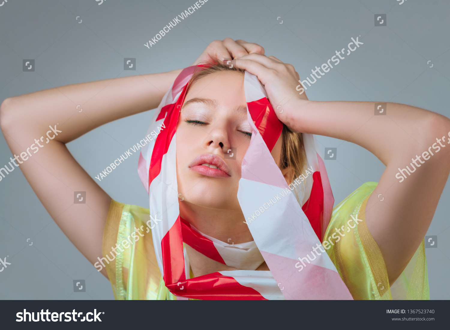 Touching her head. Close up of model touching her head and closing eyes while posing for shoot against plastic #1367523740