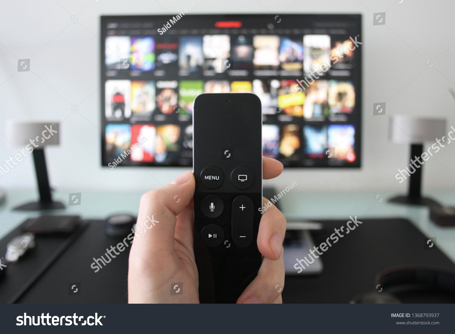 Hand holding a TV remote while watching shows on a streaming service on Television. #1368793937