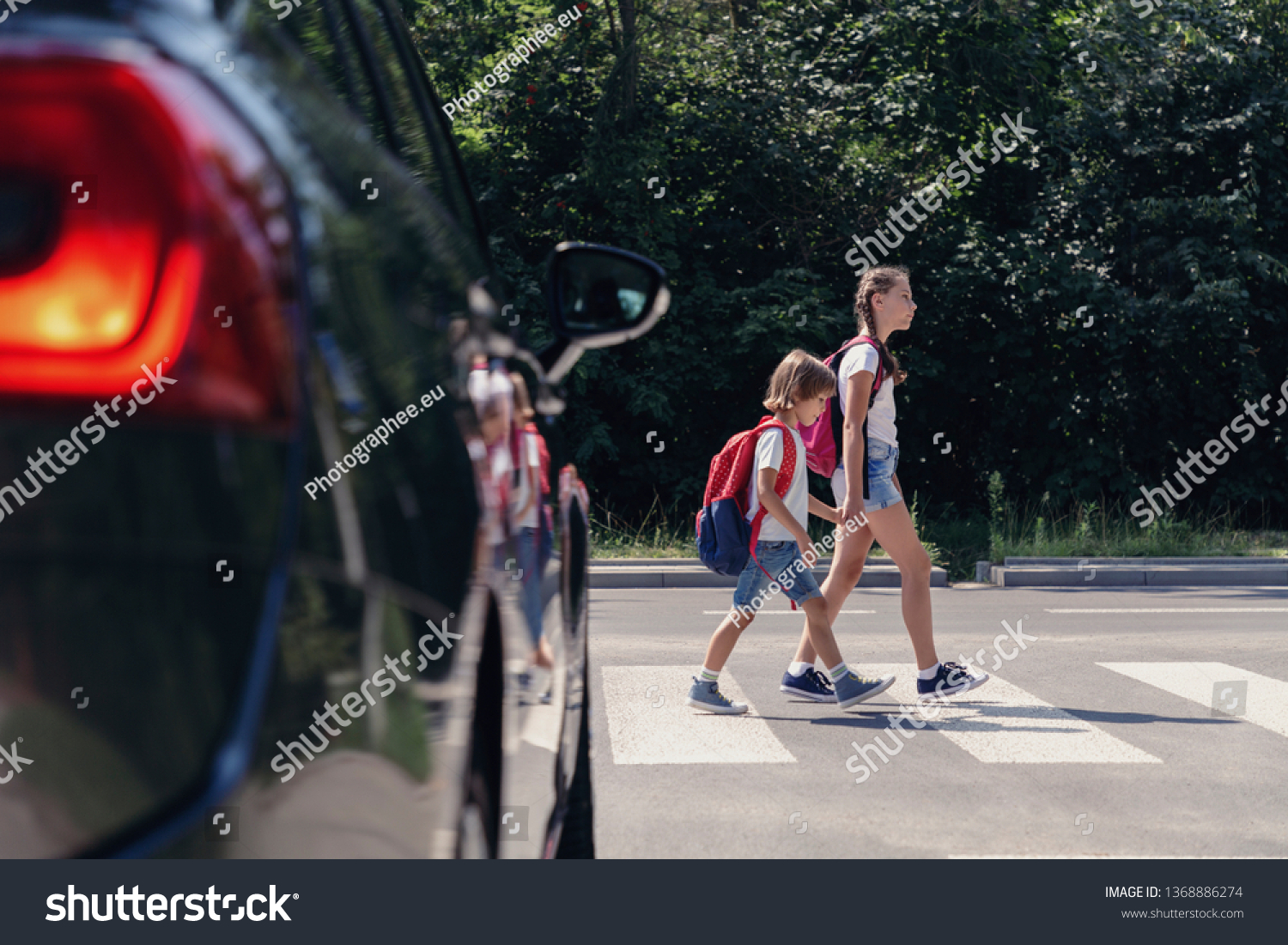 Children next to a car walking through pedestrian crossing to the school #1368886274