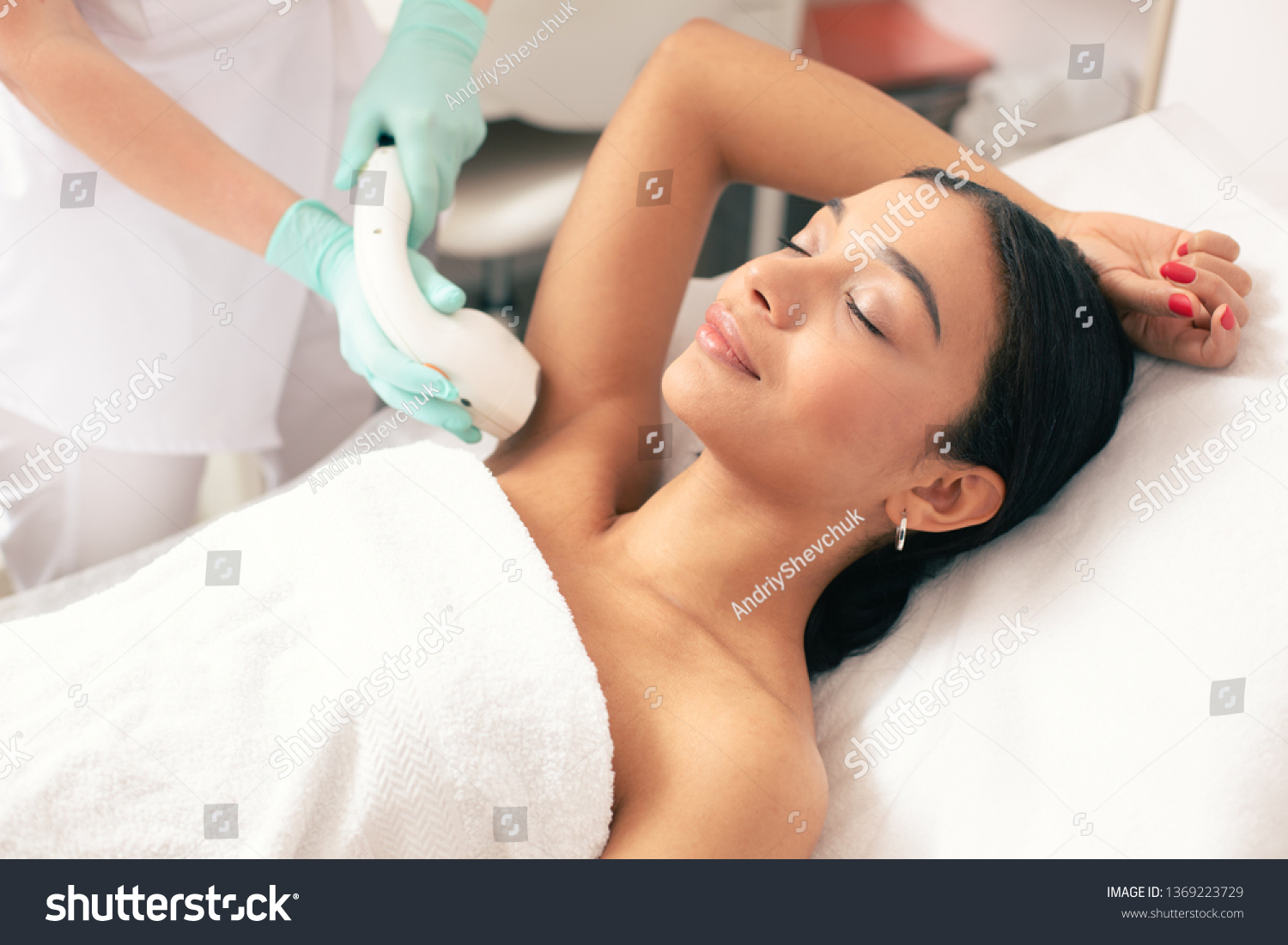 Calm young woman lying with closed eyes and putting on arm up while having laser hair removal procedure on it #1369223729
