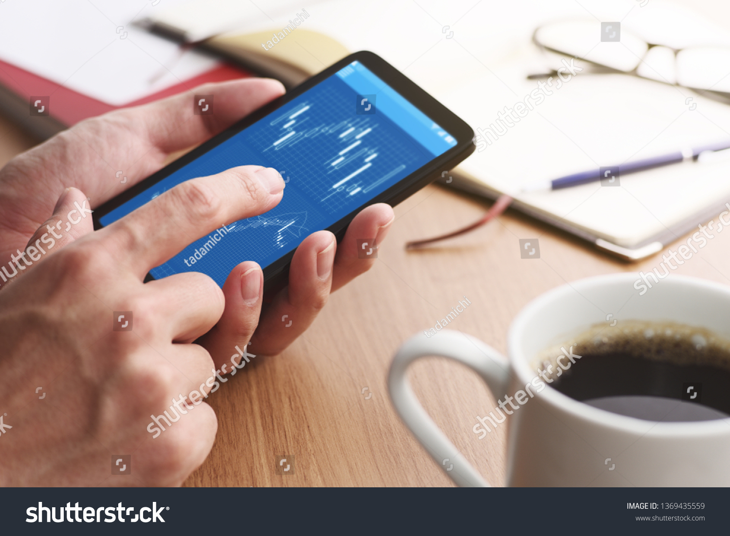Stock market charts on smartphone screen.
Closeup of male hands holding smartphone. Checking financial market.
 #1369435559