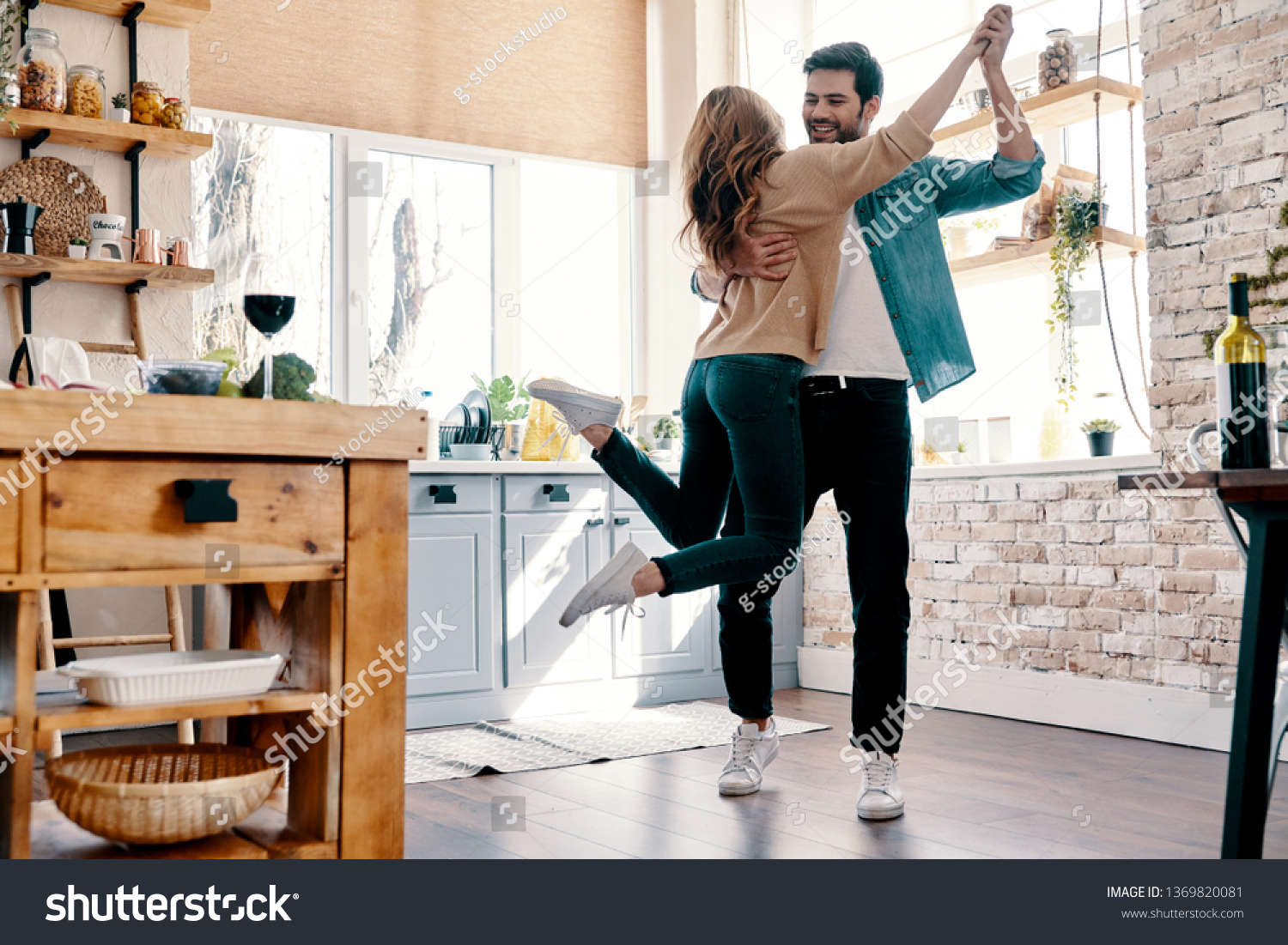 Romance. Full length of beautiful young couple in casual clothing dancing and smiling while standing in the kitchen at home #1369820081