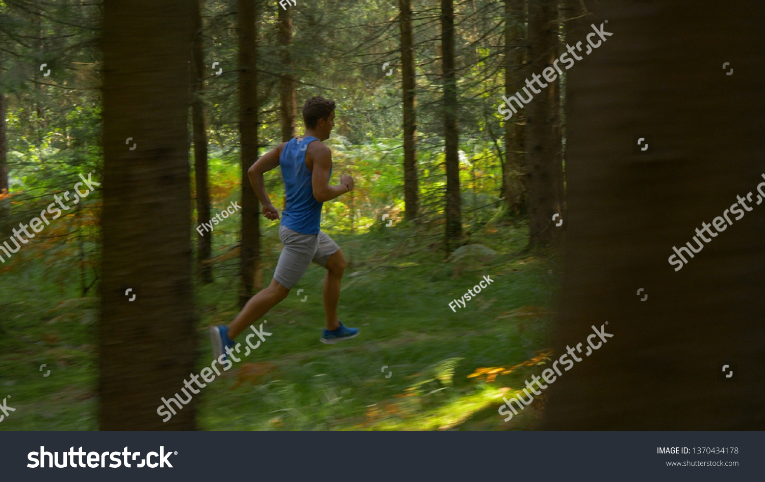 Athletic sportsman goes for a long relaxing jog along an empty forest trail on an idyllic summer day. Sporty Caucasian male exploring the tranquil wilderness by jogging through the coniferous forest. #1370434178