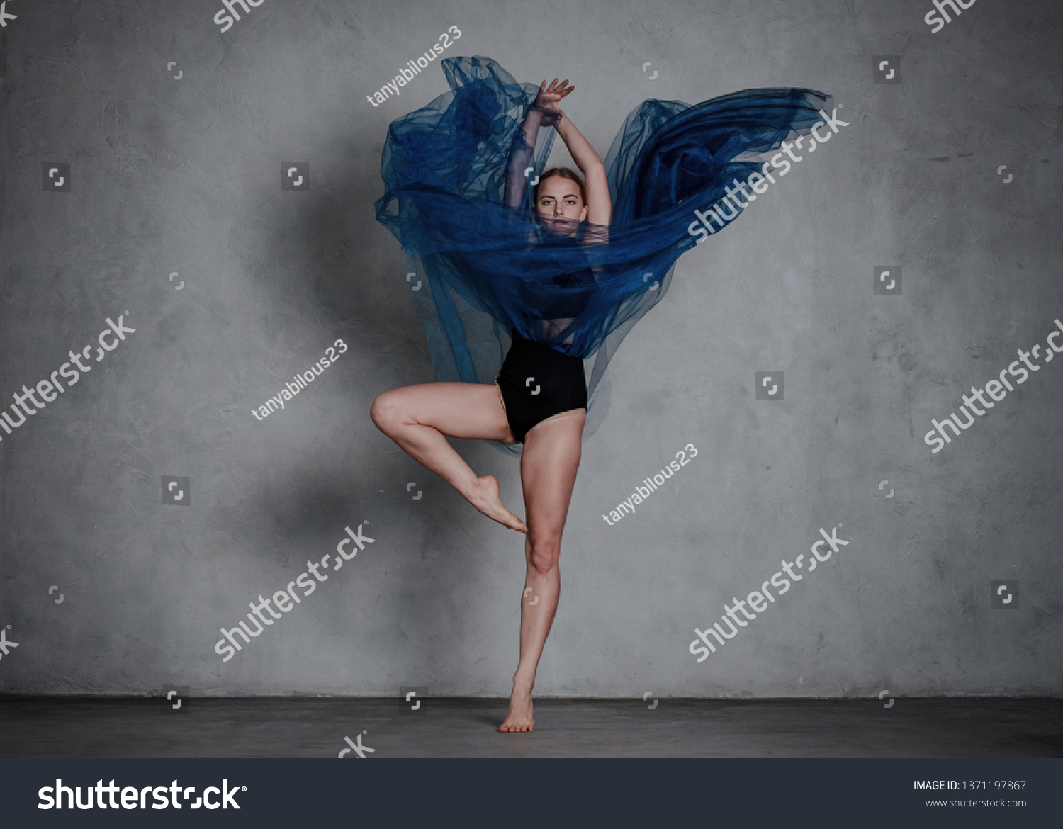 Young modern dancer in blue dress. trains and dances in a gray studio #1371197867