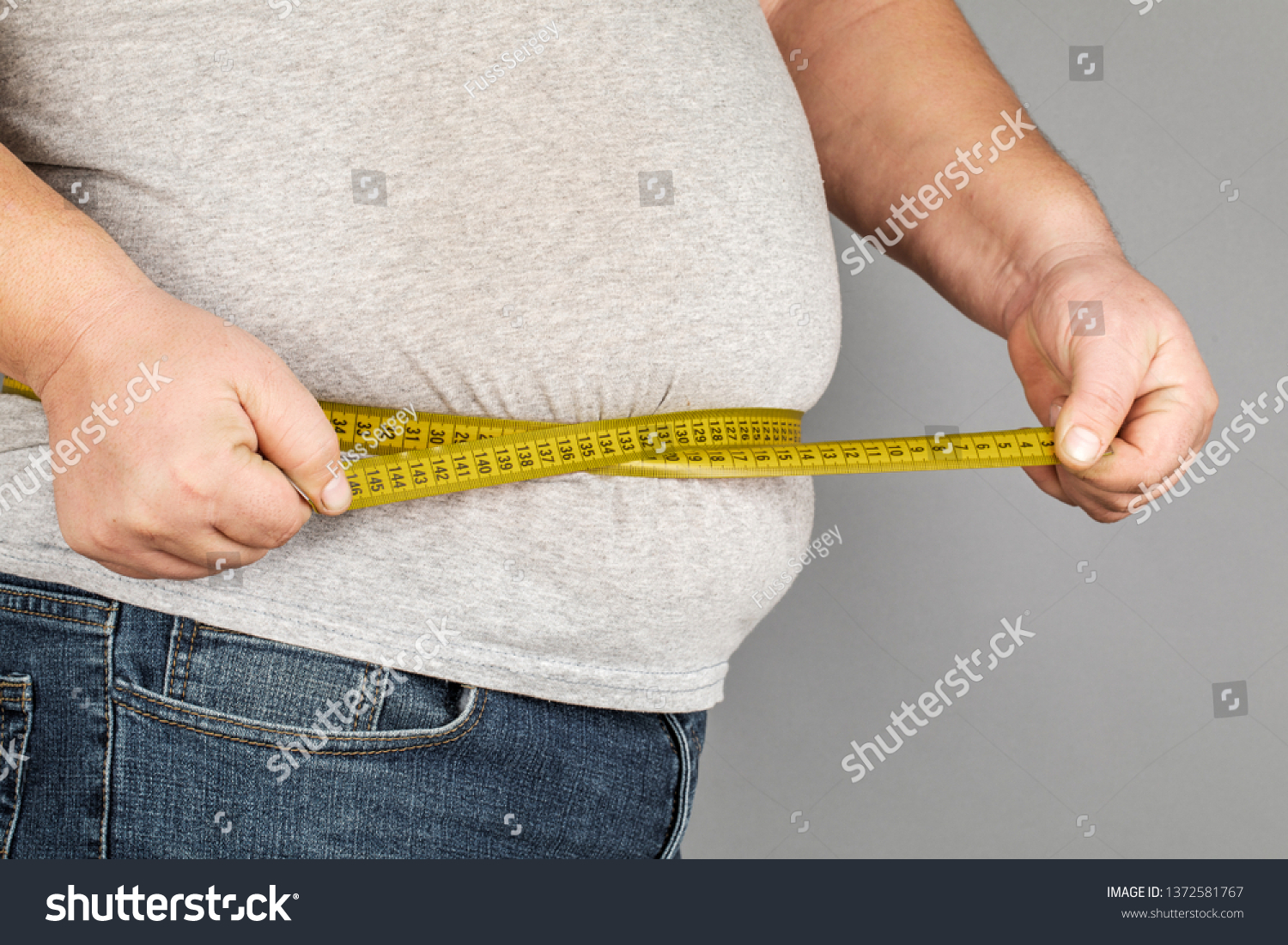A man measures his fat belly with a measuring tape. on a gray background #1372581767