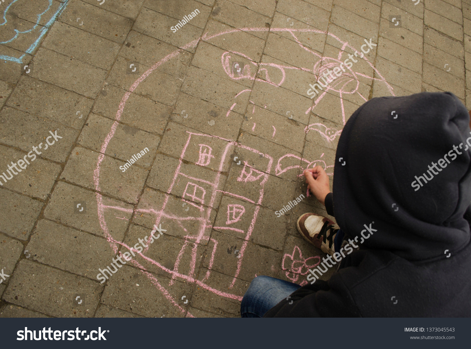 
The child draws on the pavement with colored chalk. Holiday, city day. #1373045543