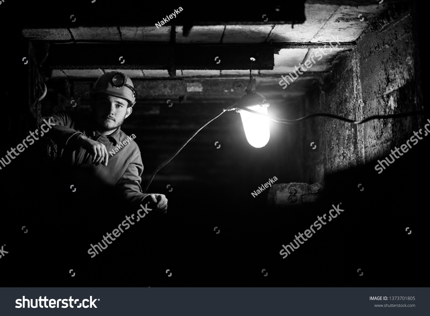 A young guy in a protective suit and helmet sits in a tunnel with a burning scrapbook. Miner in mine #1373701805