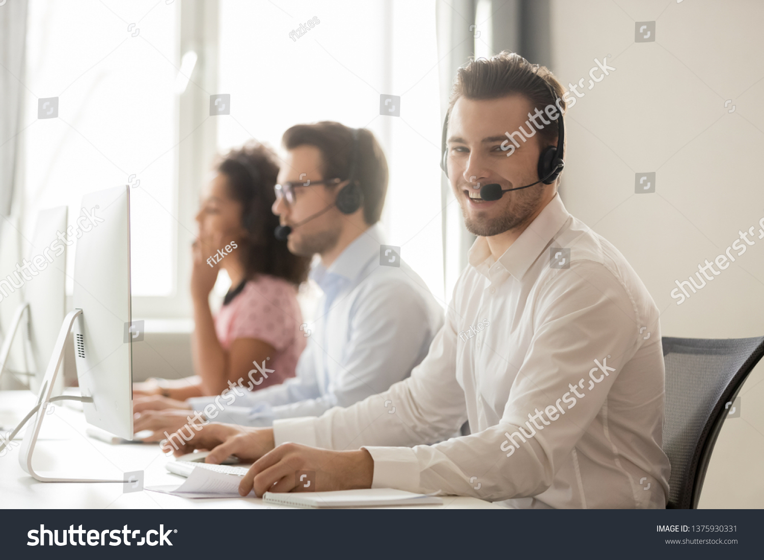 Three diverse workers service phone call center operators working wearing headset use pc, focus on smiling team member looks at camera, support everyday, opportunity to grow and develop career concept #1375930331