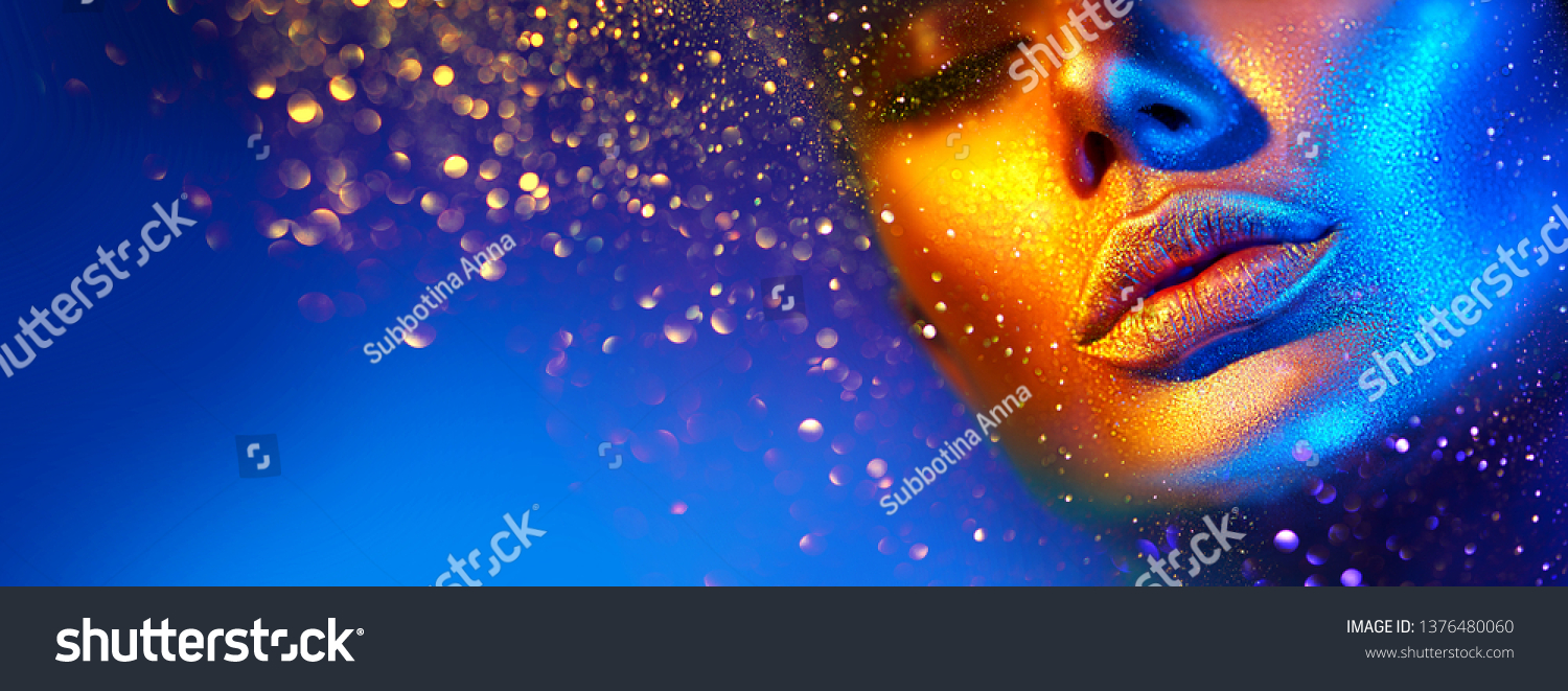 Fashion model woman skin face in bright sparkles, colorful neon lights, beautiful sexy girl lips, mouth. Trendy glowing gold skin make-up. Art design make up. Glitter metallic shine golden blue makeup #1376480060