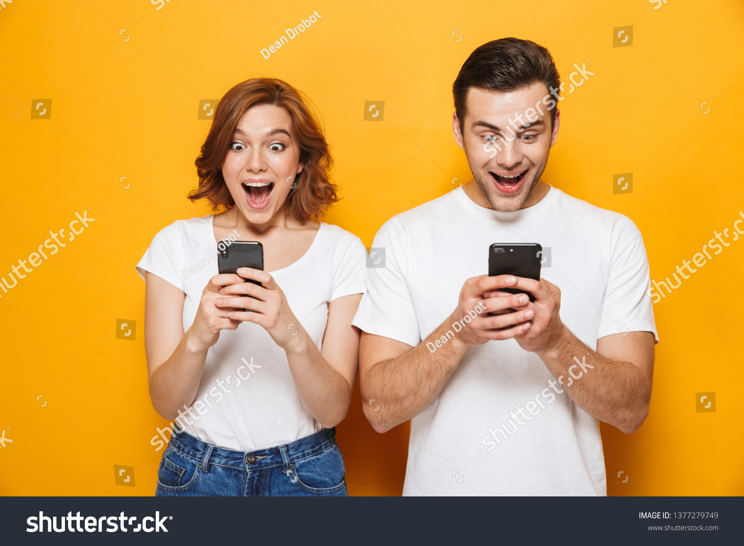 Portrait of a cheerful young couple standing isolated over yellow background, using mobile phones #1377279749