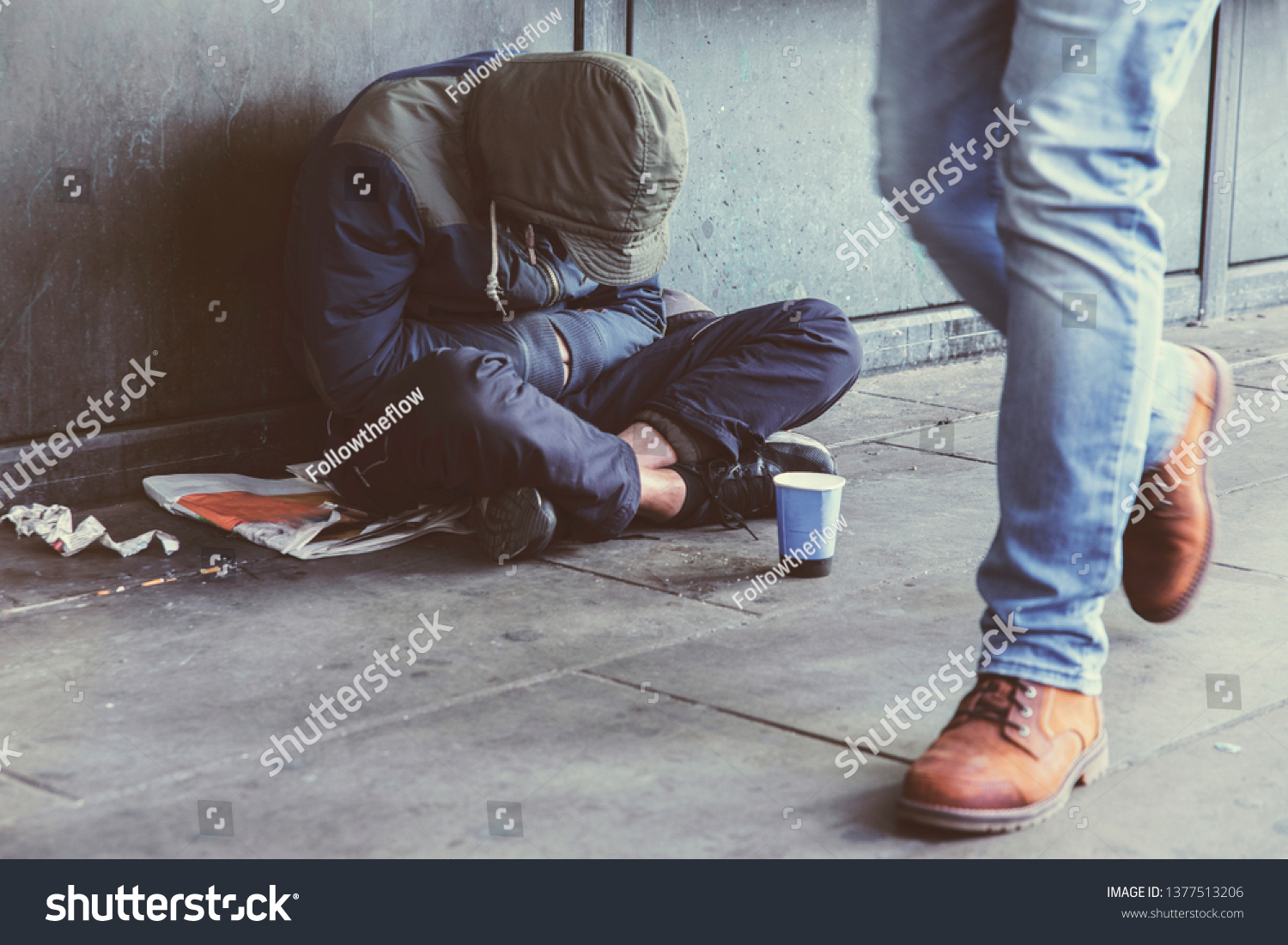Homeless adult man sitting on the street in the shadow of the building and begging for help and money. Problems of big modern cities. Indifference of people. Social issues. #1377513206