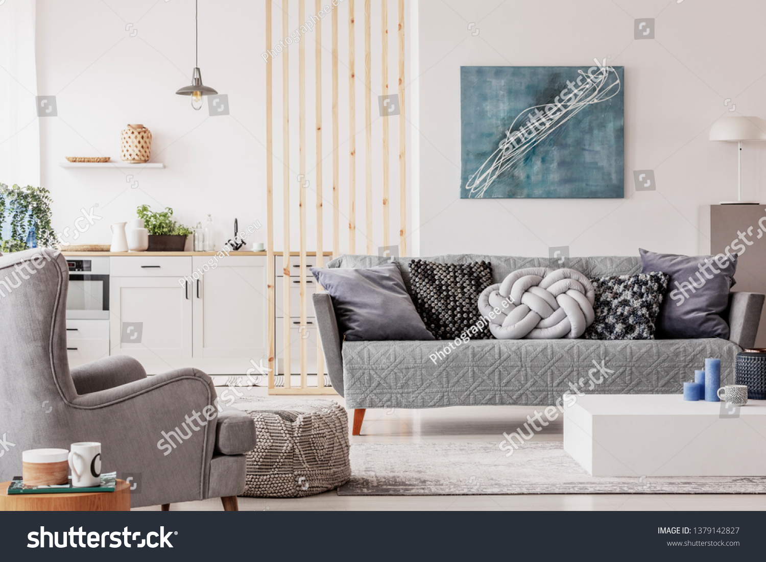 Open plan studio apartment with small white kitchen and living room with grey couch and wooden coffee table #1379142827