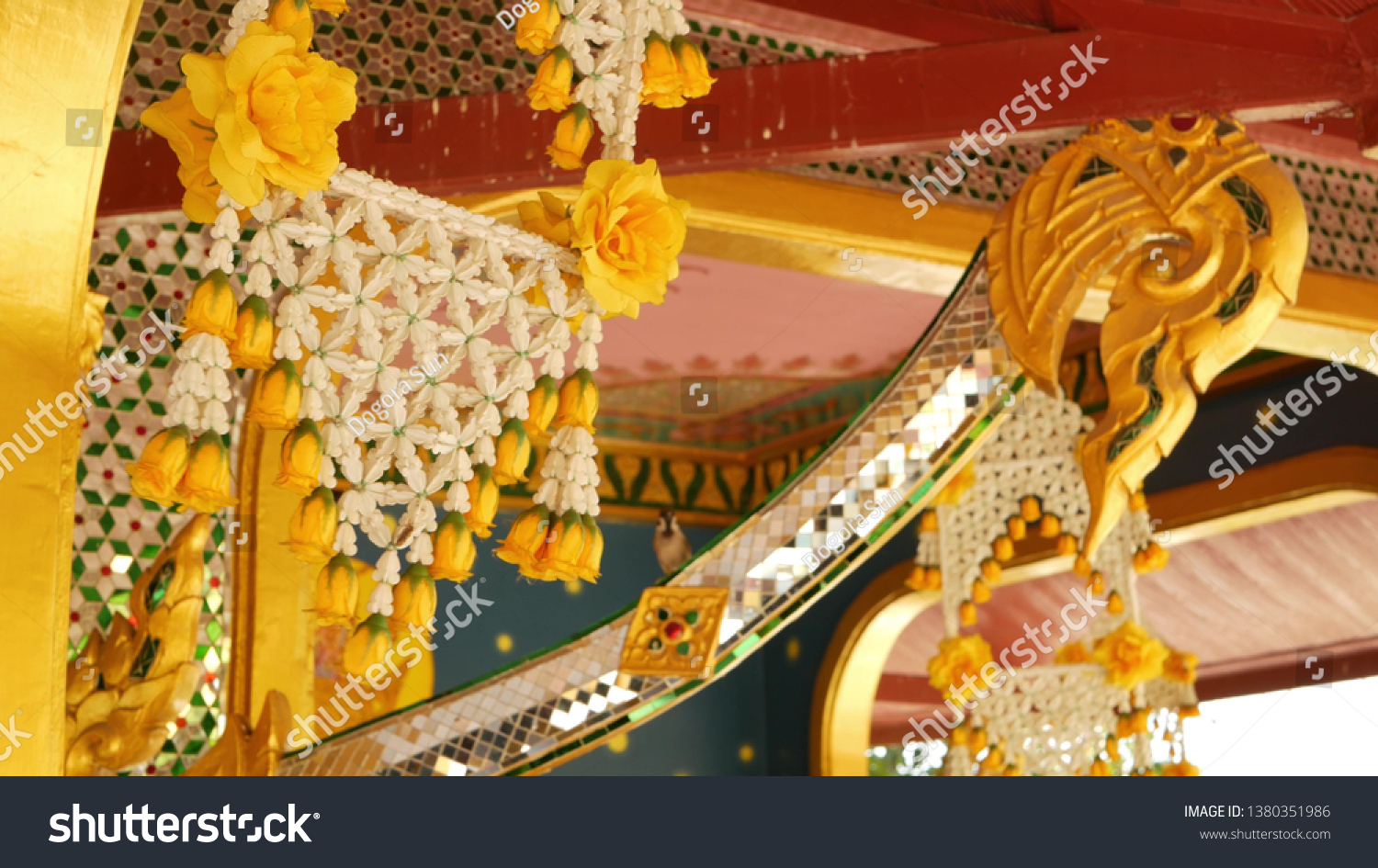 Floral interior decorations of oriental building. Beautiful flower compositions hanging on ceiling of ornamental building of buddist temple on sunny day in Thailand. #1380351986