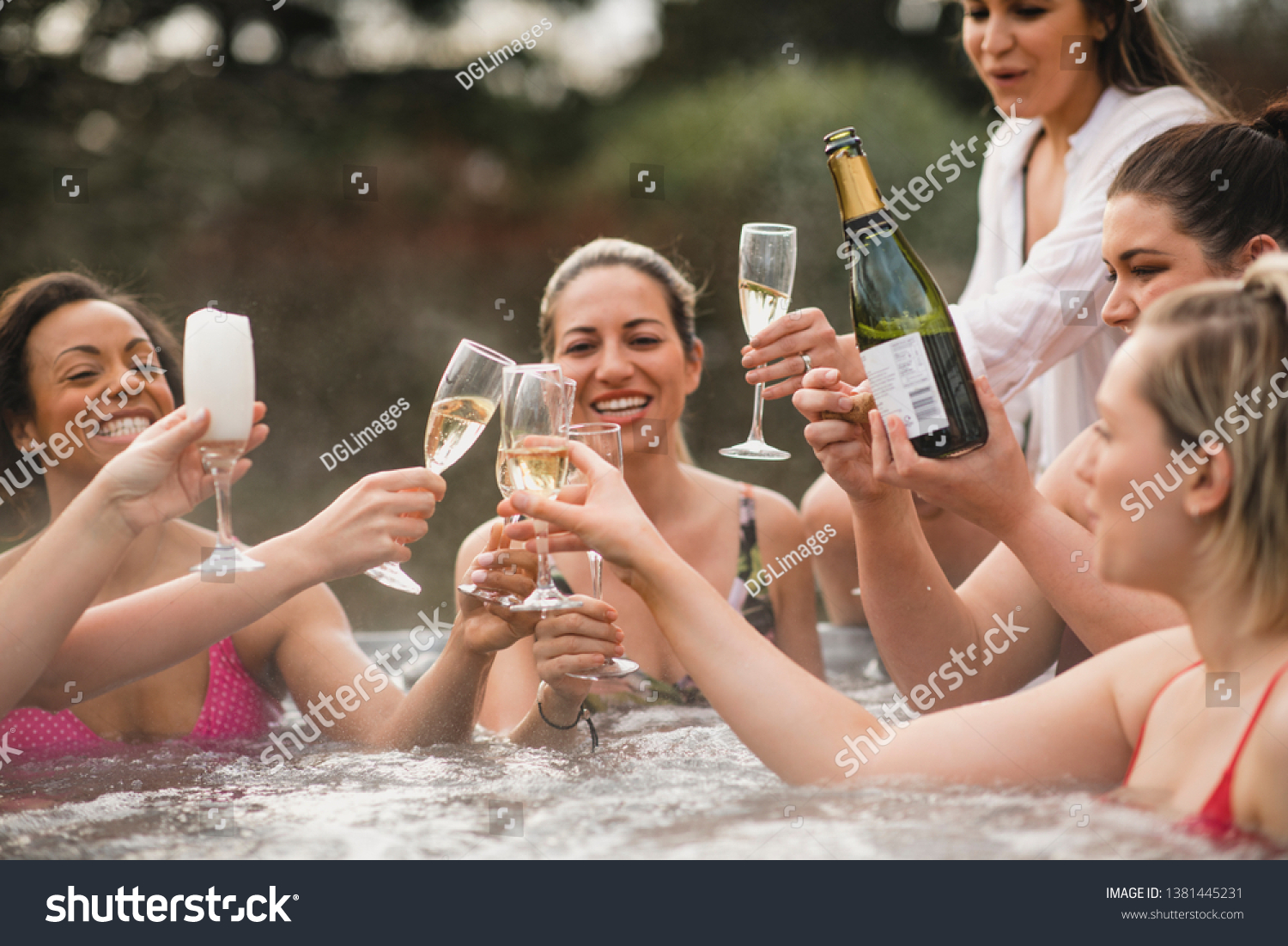 Small group of female friends socialising and relaxing in the hot tub on a weekend away. They are celebrating with a glass of champagne. #1381445231