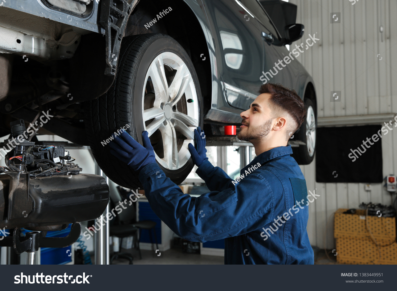 Technician checking car on hydraulic lift at automobile repair shop #1383449951