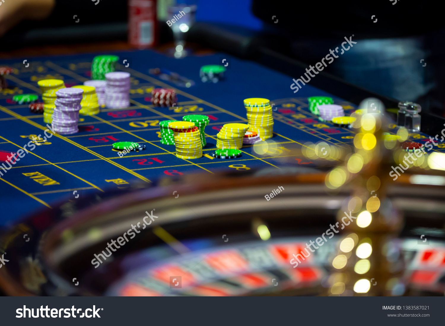 Roulette table with human hands putting down chips in casino. Roulette wheel in the foreground. Gamble game. Unrecognizable people. #1383587021