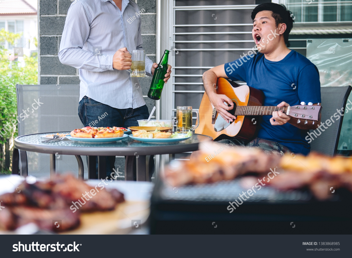 Group of friends Two young man enjoying grilled meat and play guitar with raise a glass of beer to celebrate the holiday festival happy drinking beer outdoors and enjoyment at home. #1383868985