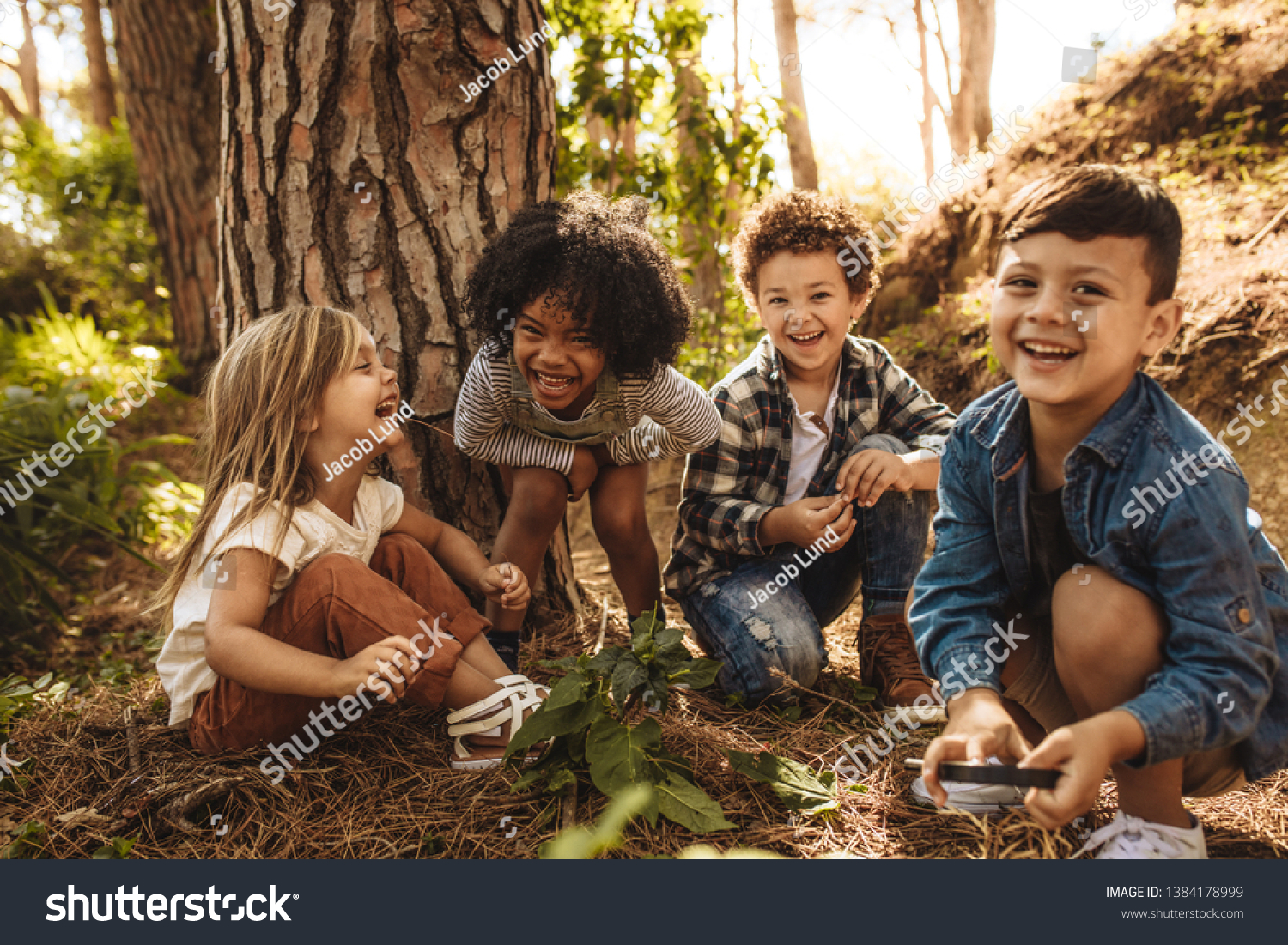 Group of cute kids sitting together in forest and looking at camera. Cute children playing in woods. #1384178999