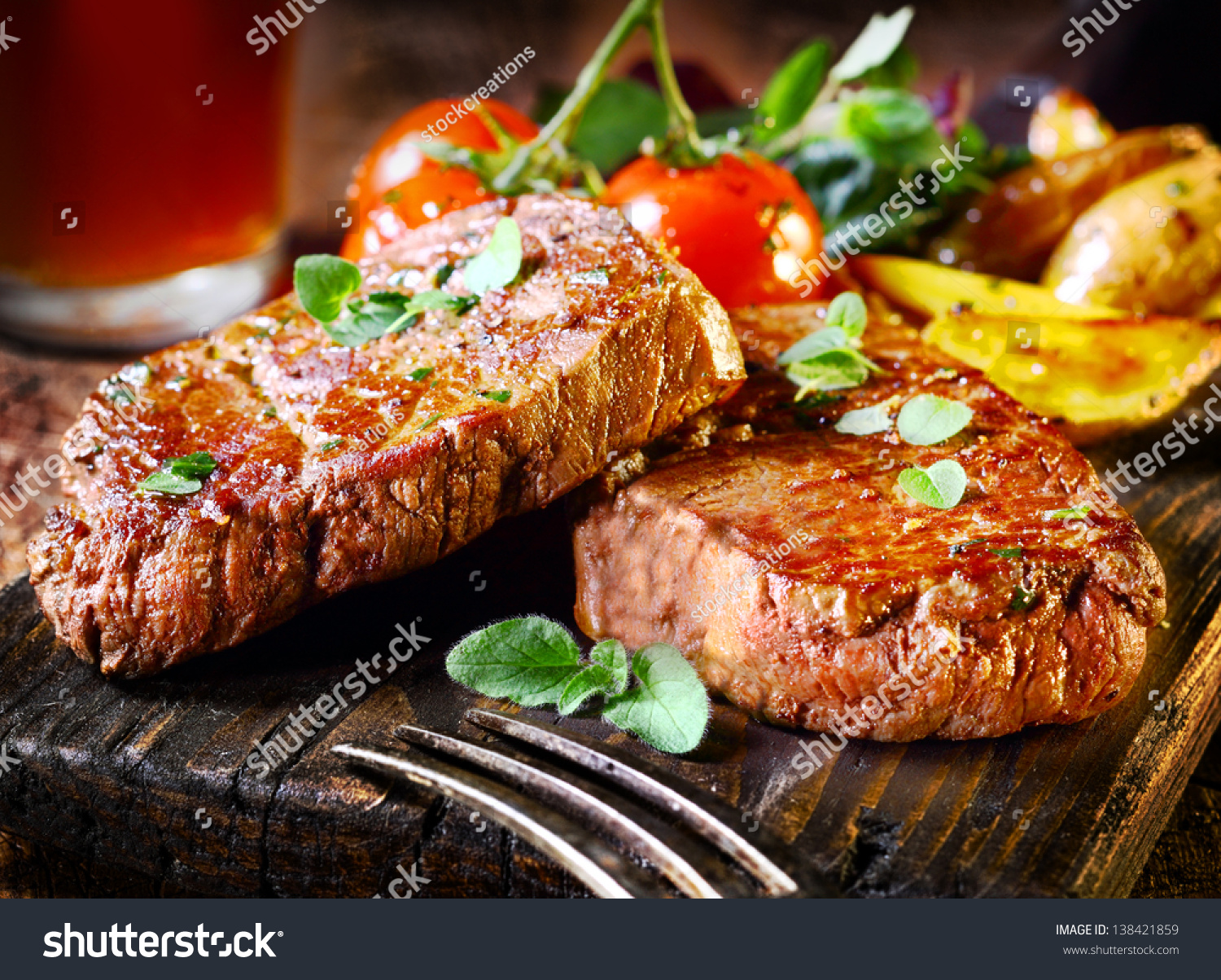 Succulent thick juicy portions of grilled fillet steak served with tomatoes and roast vegetables on an old wooden board #138421859