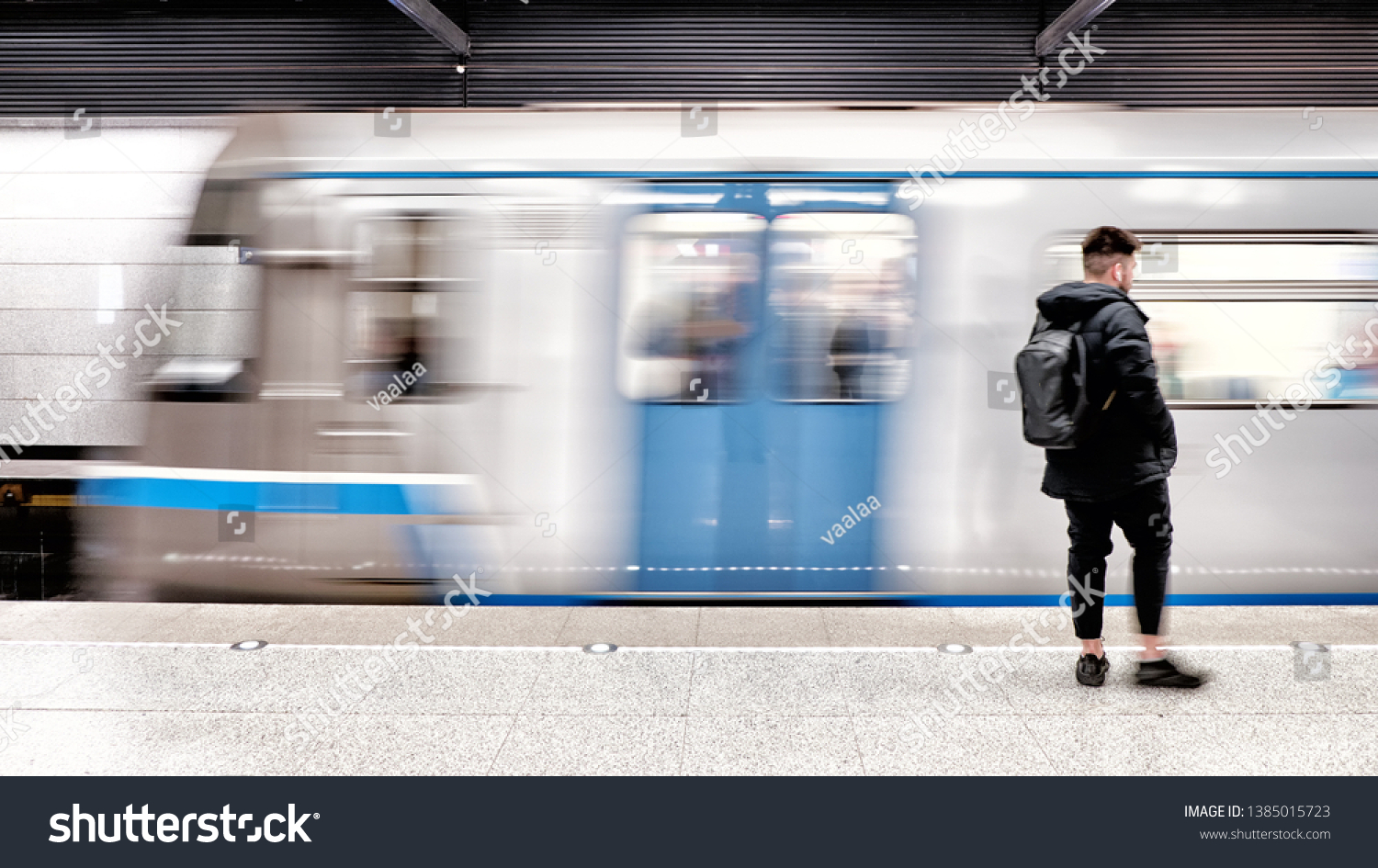 subway train arriving to modern metro station with male passenger person waiting on platform blurred background side view of city transportation underground station with motion car and people #1385015723