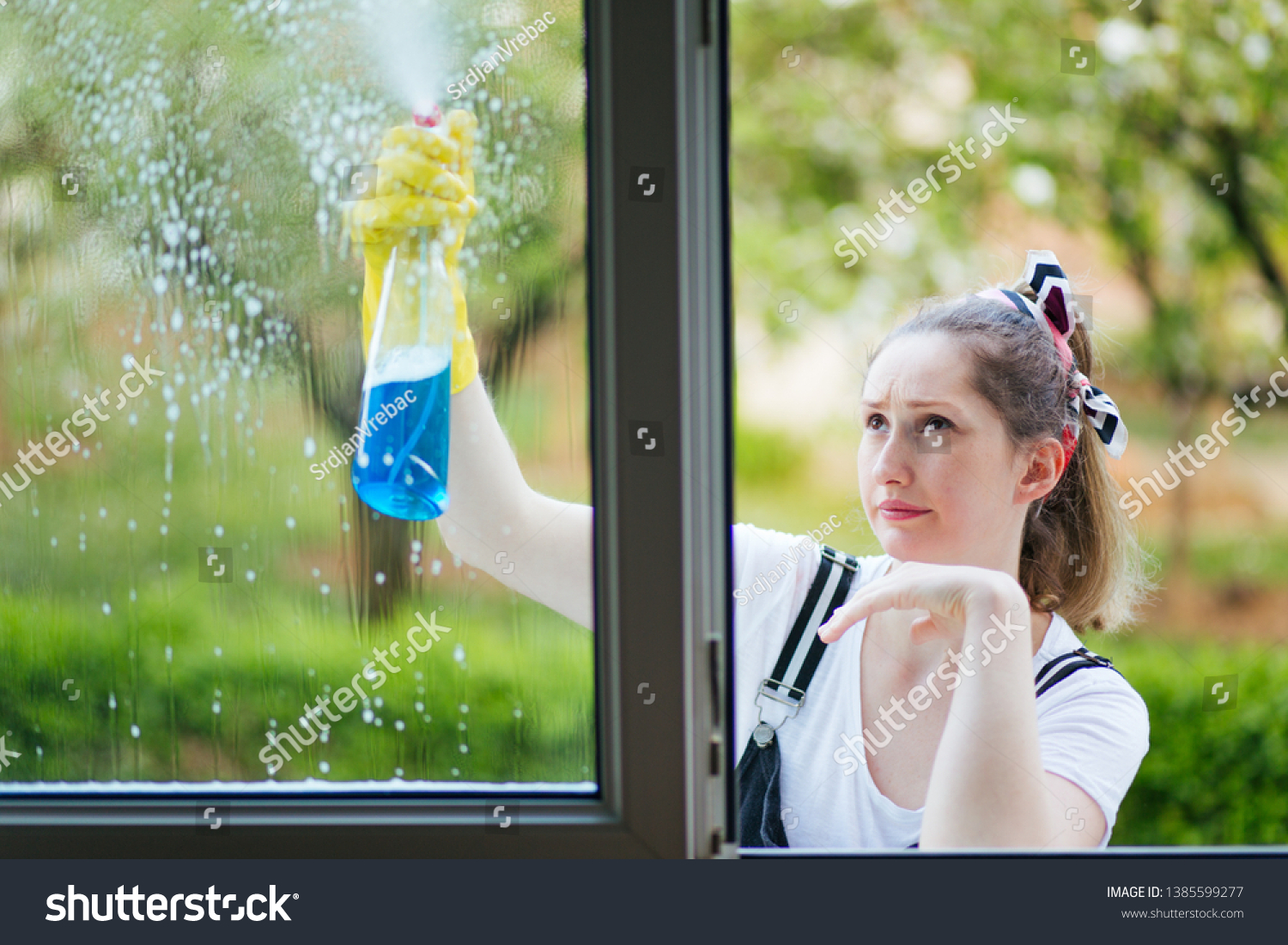 Young funny housewife cleaning windows with spray detergent. housework concept. #1385599277