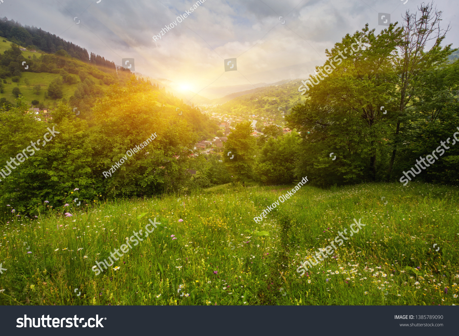 Panoramic view of beautiful landscape in the Alps with fresh green meadows and blooming flowers and snow-capped mountain tops in the background on a sunny day with blue sky and clouds in springtime. #1385789090
